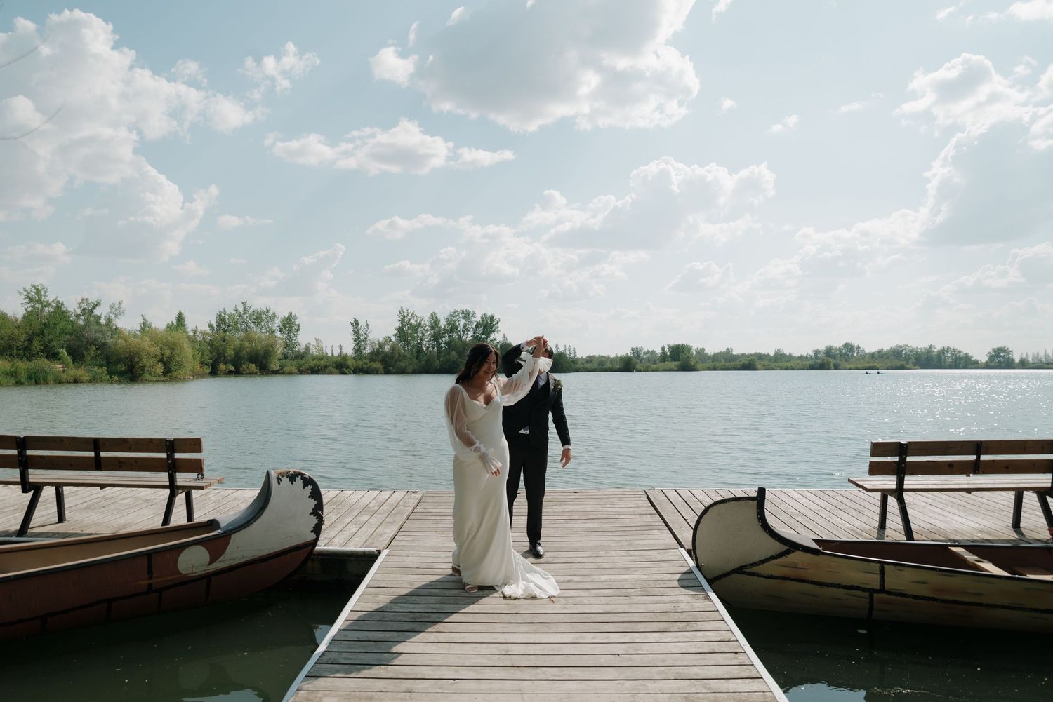 A scenic lakeside dock stretches out over calm waters under a bright blue sky.