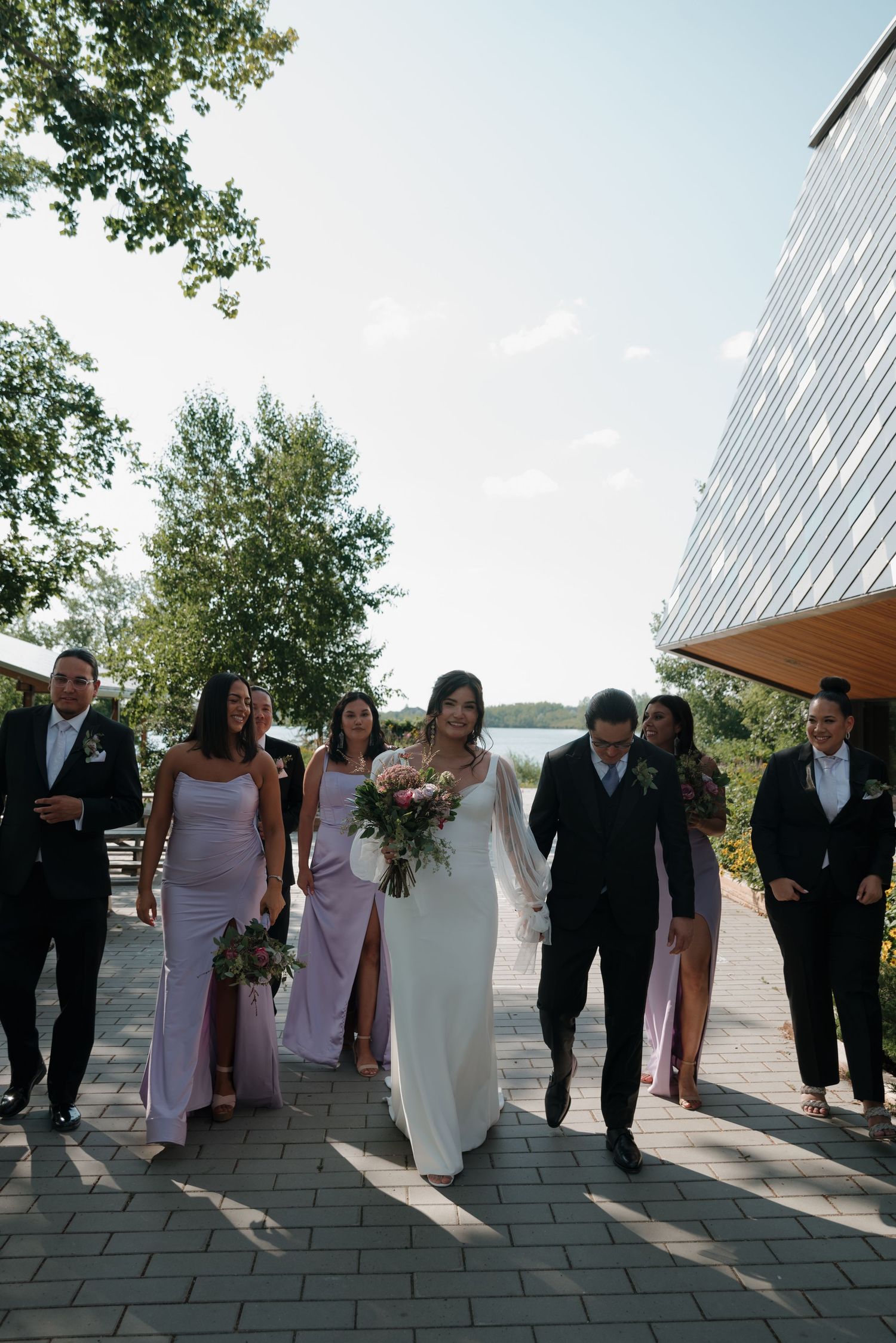 Wedding party processes along a modern architectural pathway with water views.