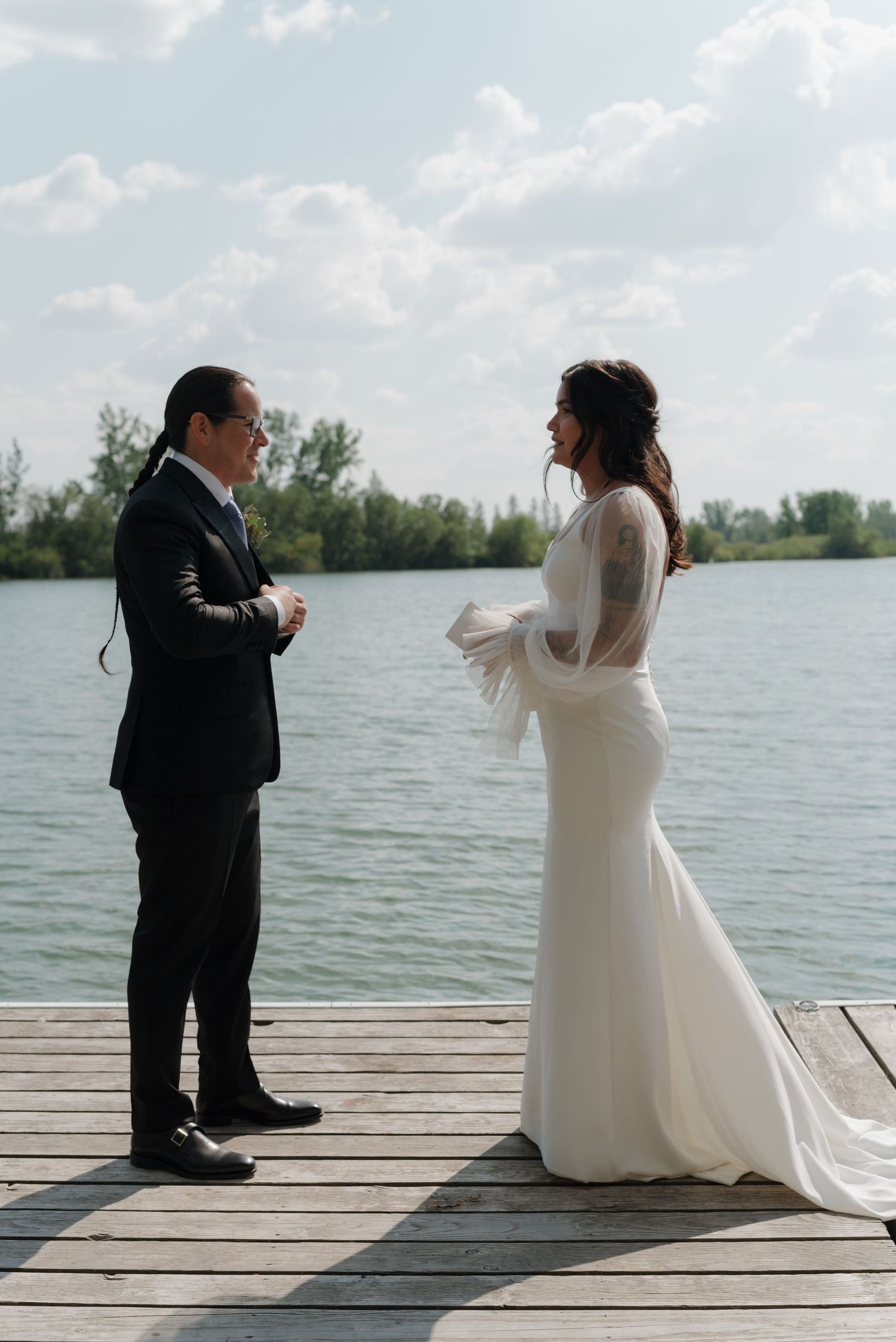 A couple shares an intimate moment on a lakeside dock during their wedding photoshoot.
