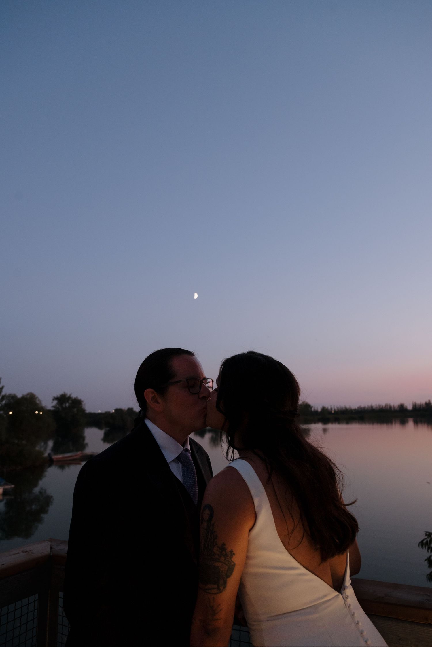 A romantic sunset silhouette scene by a tranquil lake with a couple sharing an intimate moment on the dock.
