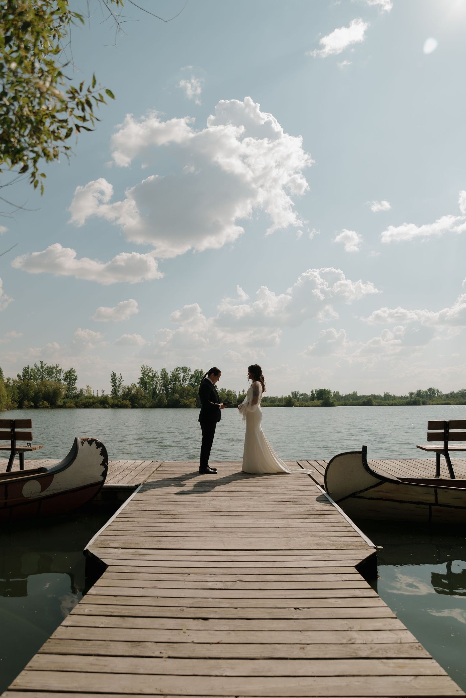 A serene wooden dock extends over a tranquil lake with benches and boats visible in the distance.