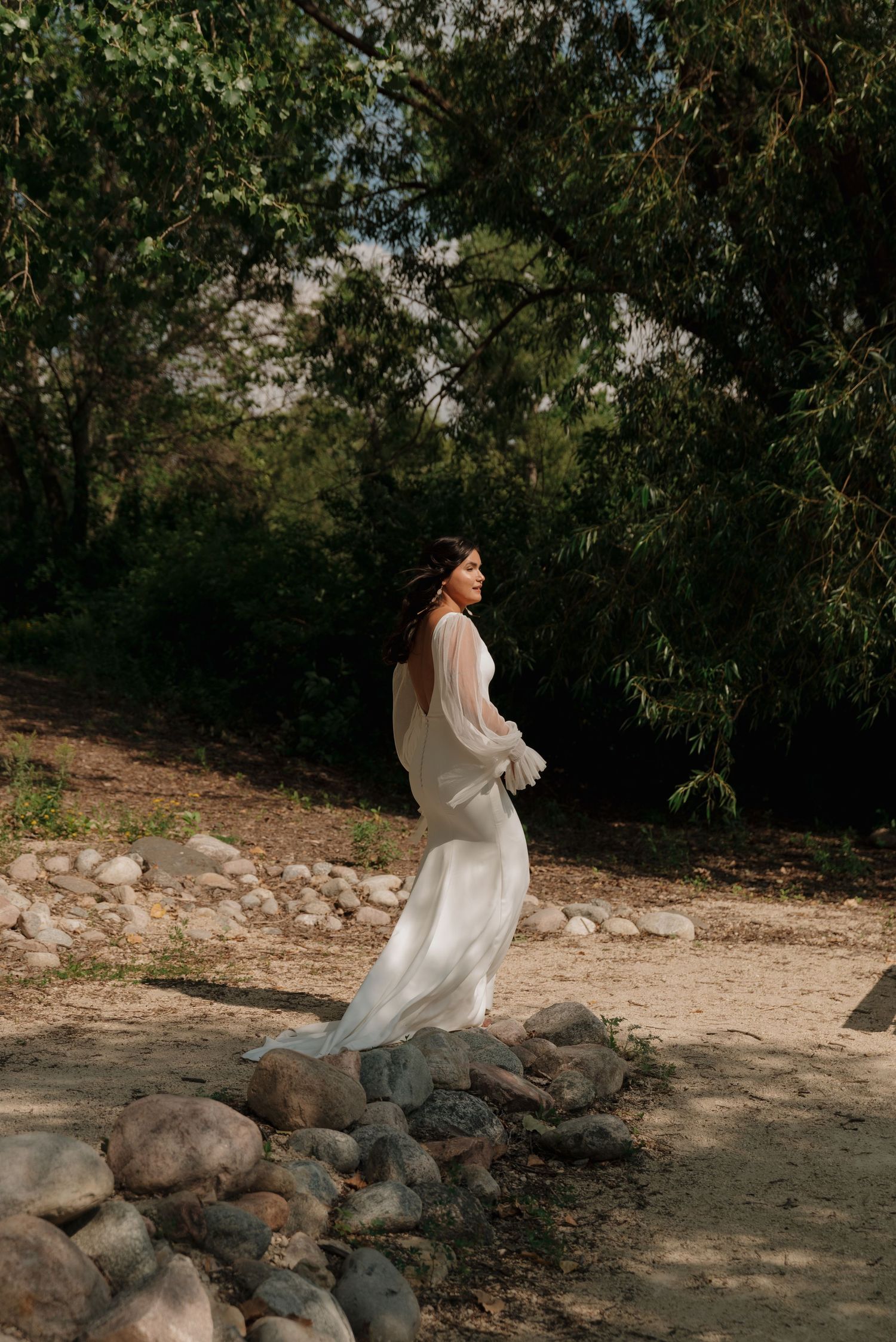 A flowing white wedding dress twirls gracefully against a natural backdrop with rocks and trees.