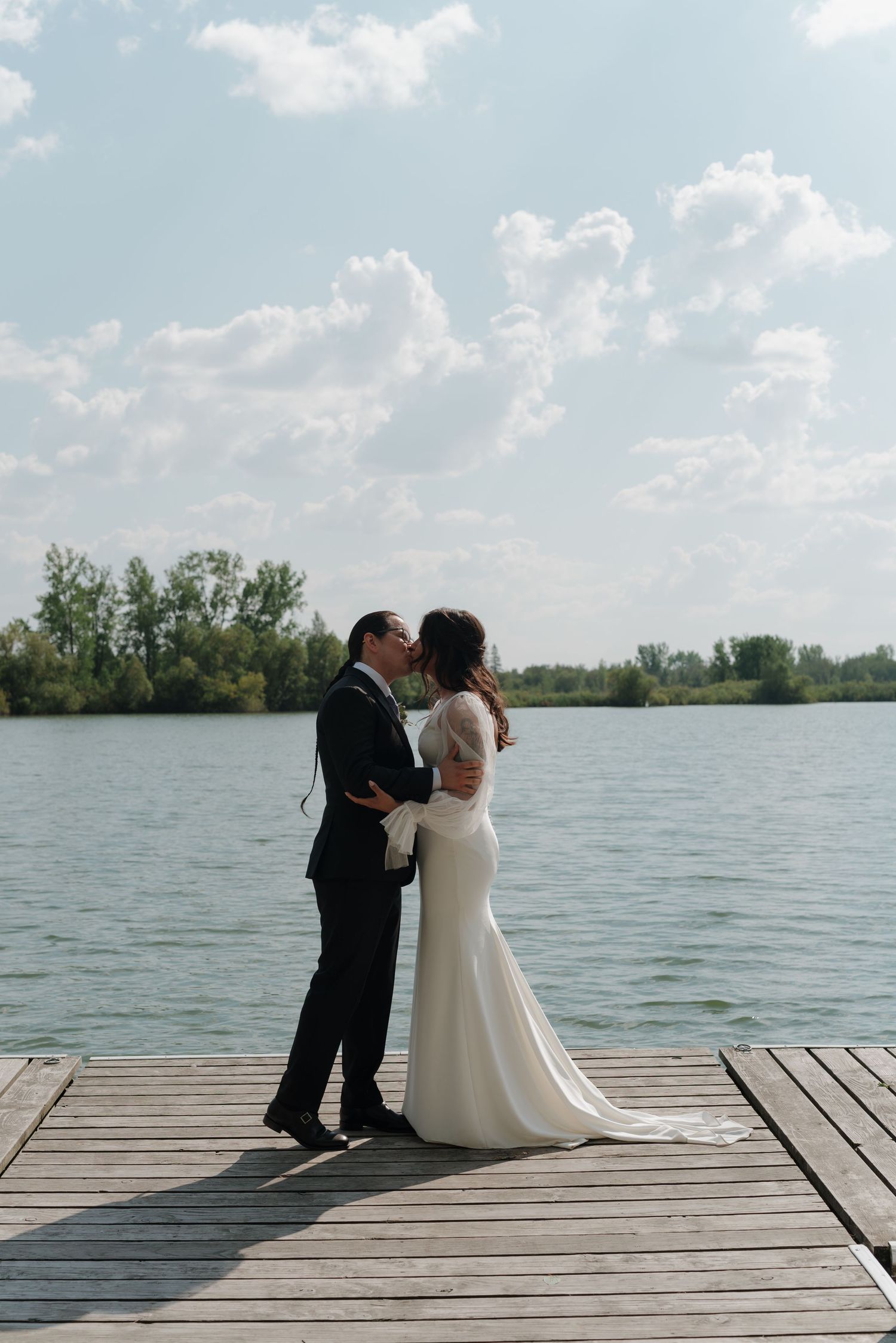A romantic wedding moment captured on a wooden dock overlooking a peaceful lake.