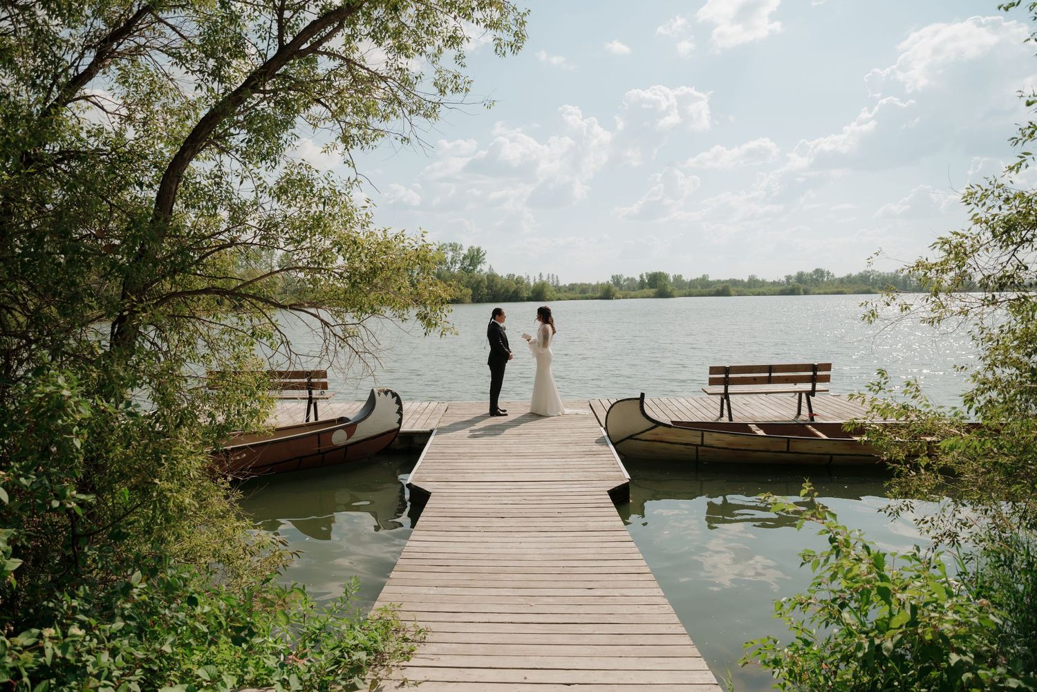 A long wooden pier stretches across a scenic lake surrounded by lush greenery.