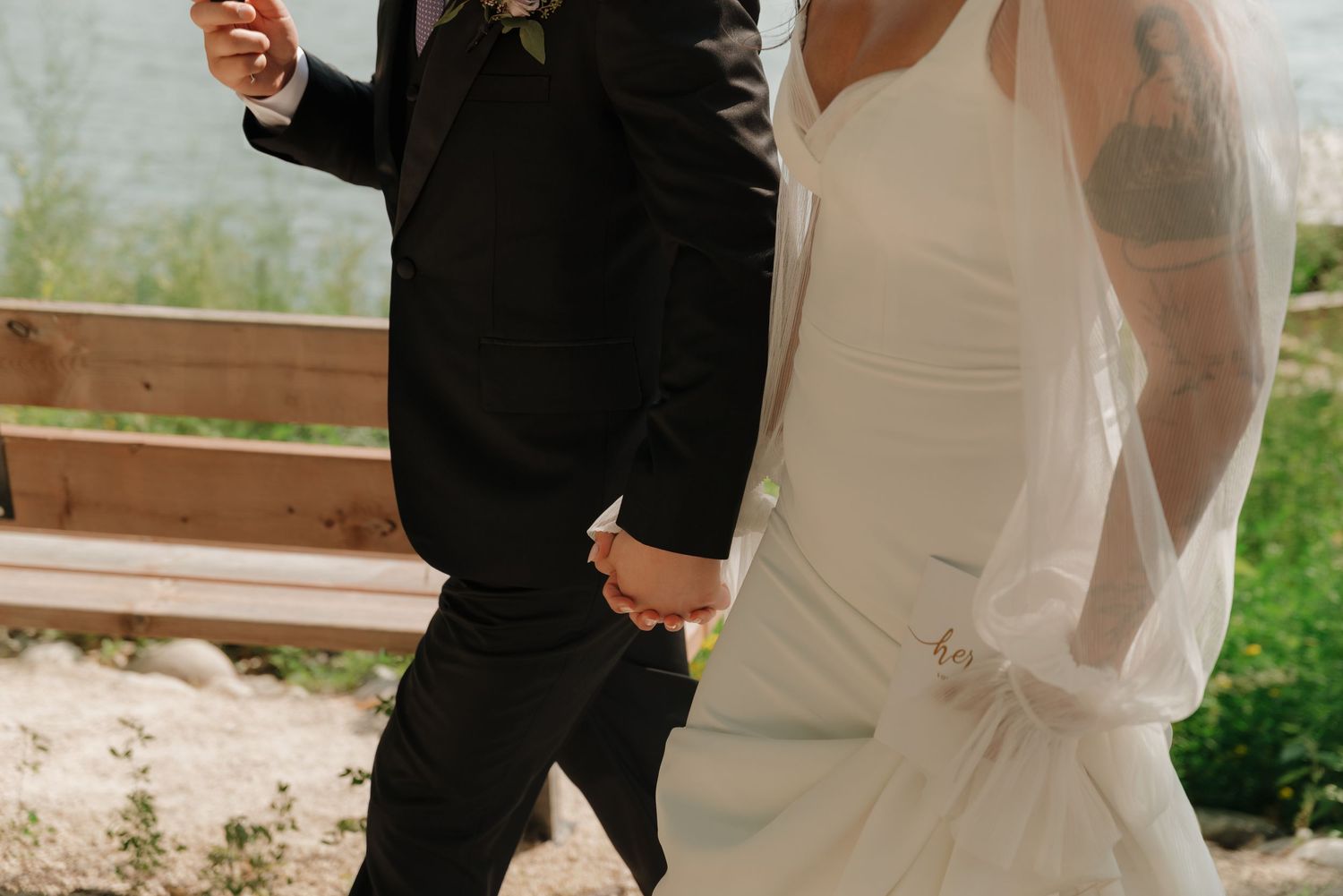 A couple in black and white attire photographed from behind on a lakeside dock during a special occasion.
