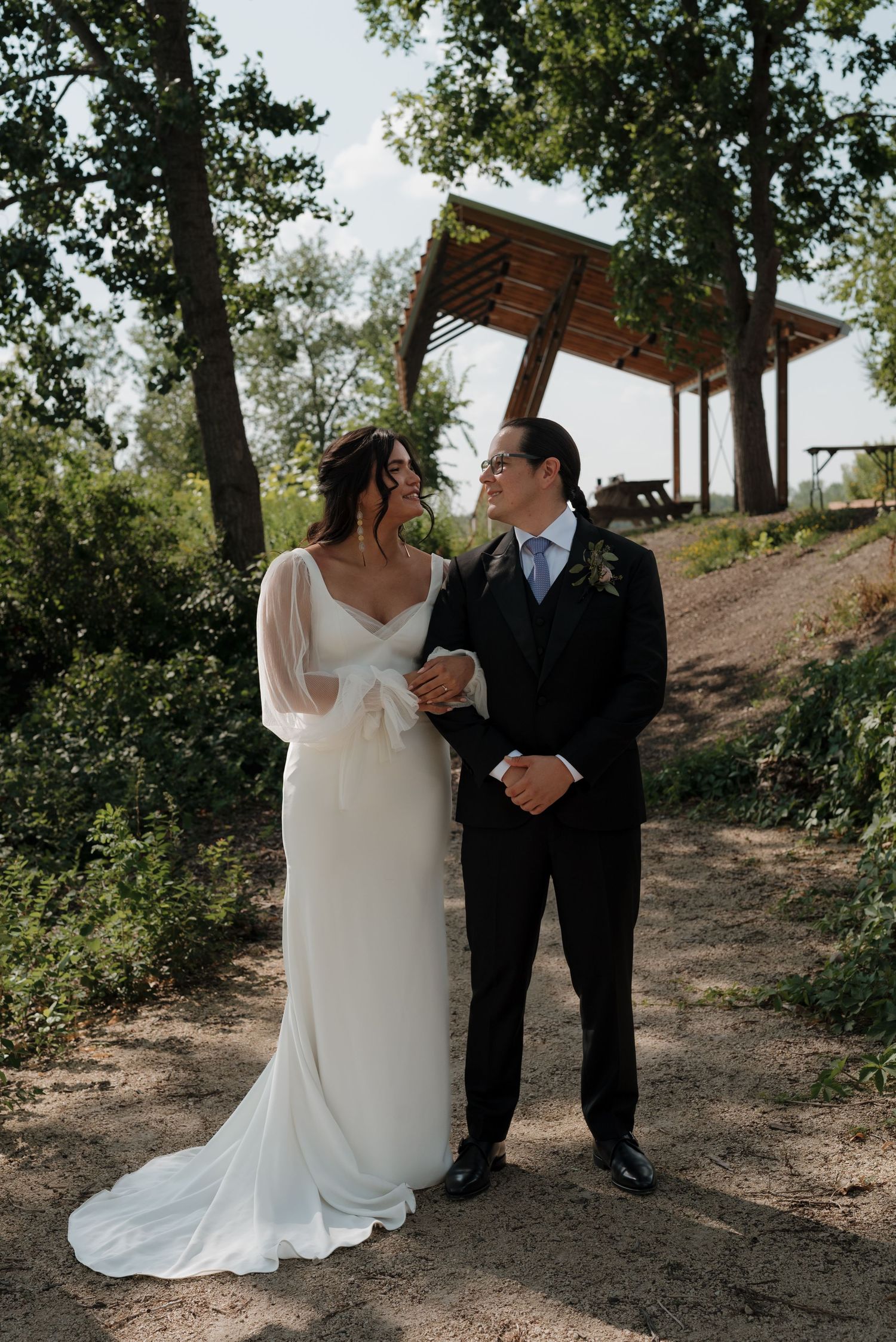 A couple shares an intimate moment during their outdoor wedding photoshoot near a wooded area.