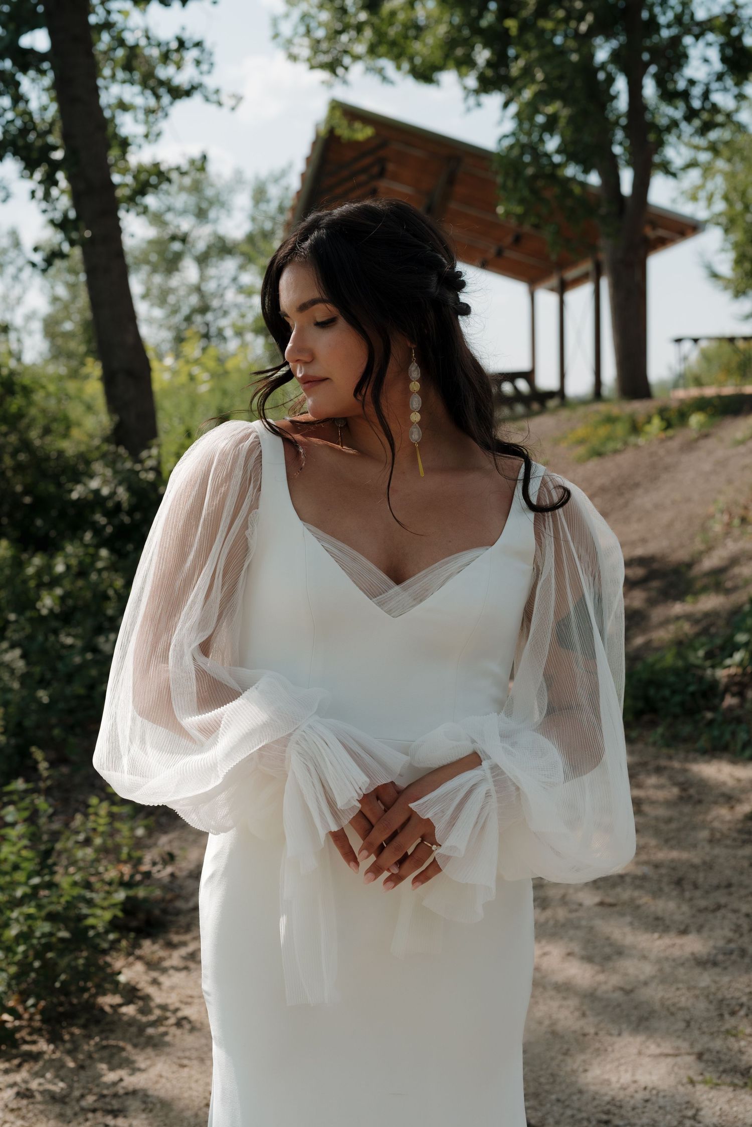 Wedding dress with flowing sheer sleeves and white fabric in natural outdoor setting.