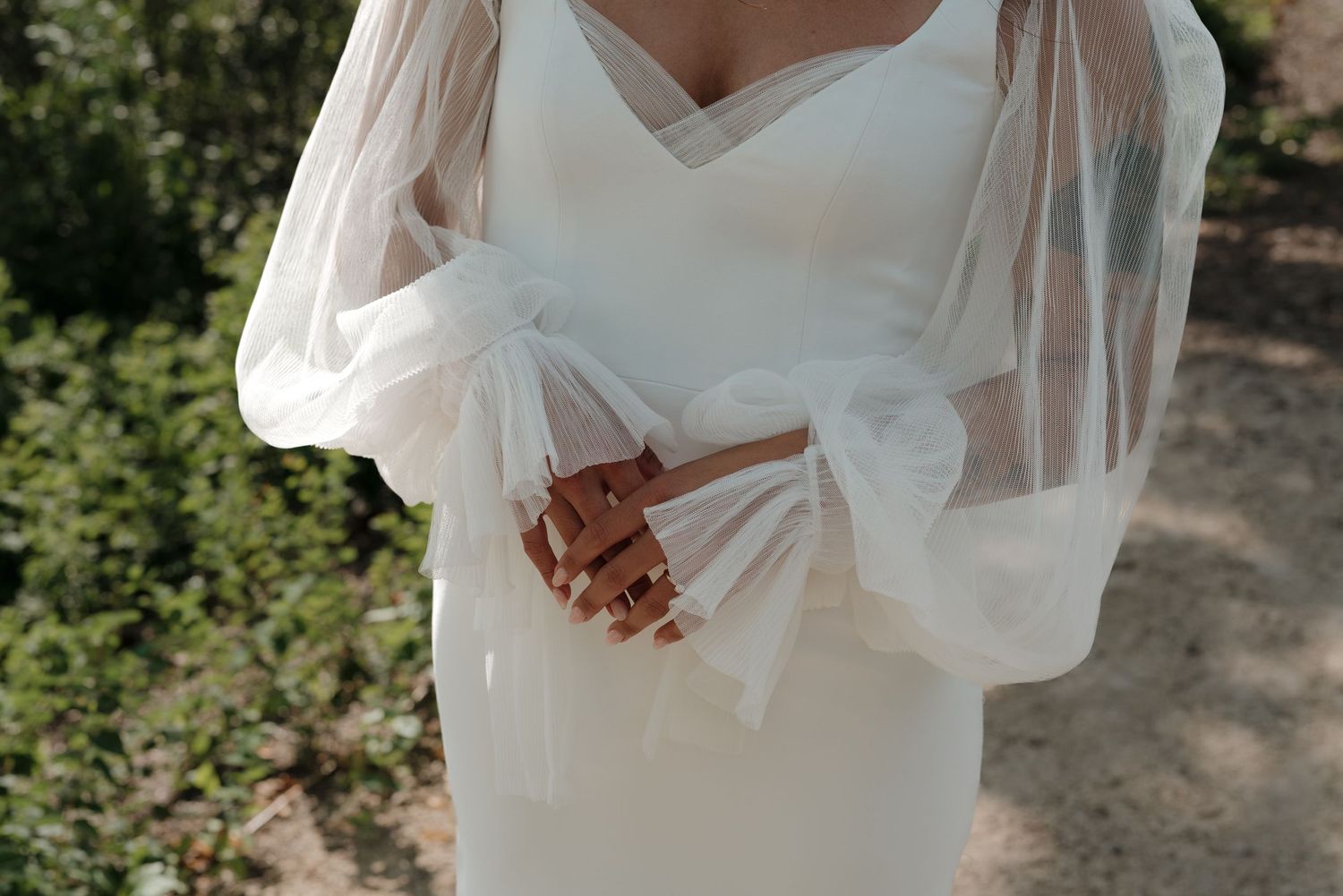 Close-up details of a white wedding dress with delicate lace and flowing fabric in natural outdoor lighting.