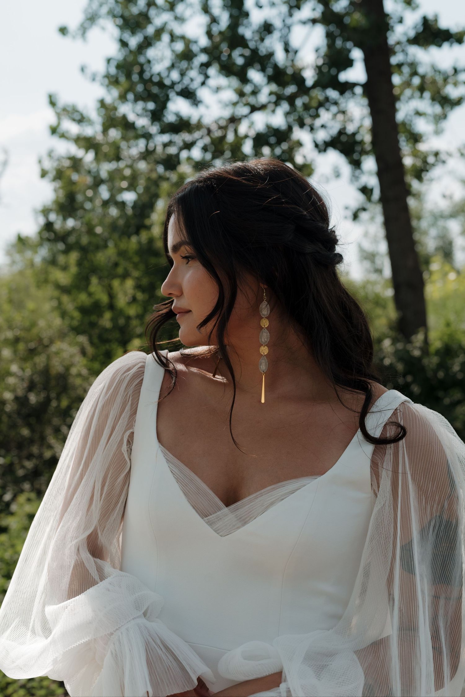 Elegant bridal portrait showing romantic sheer sleeves and V-neck neckline against natural backdrop.