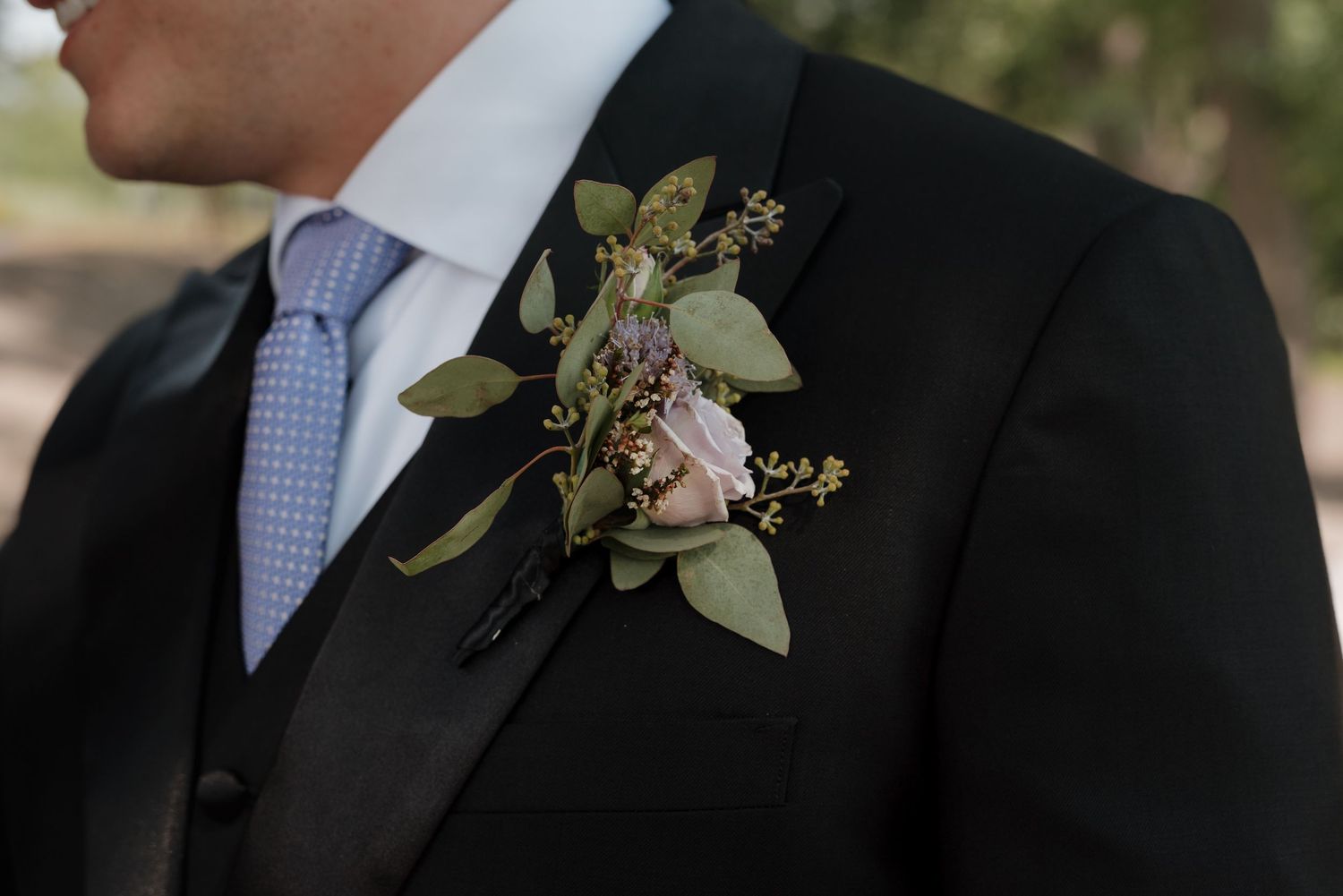 Close-up of boutonniere with delicate flowers pinned to black suit lapel.