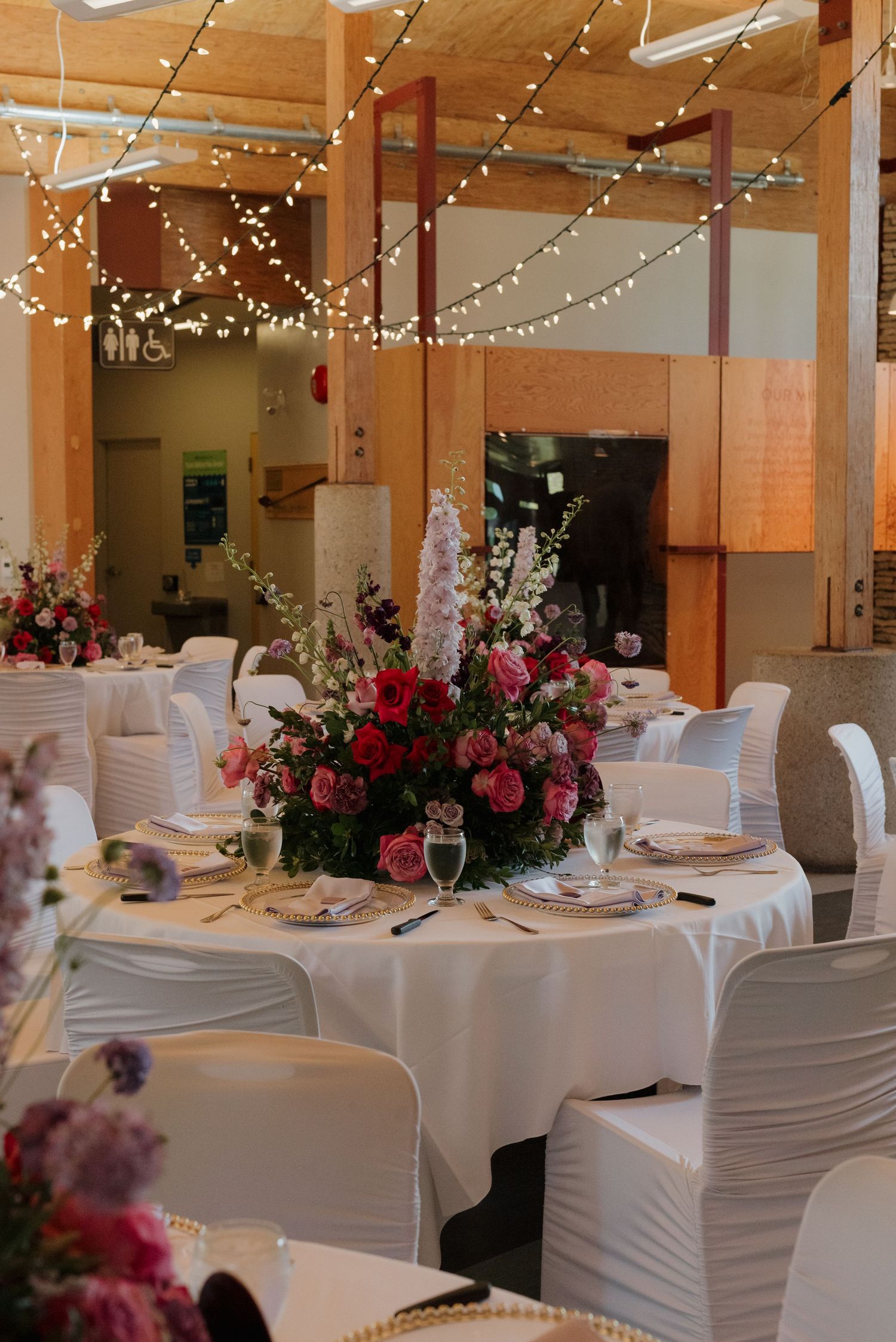 Elegant wedding reception venue with white chair covers and pink floral centerpieces under twinkling string lights.