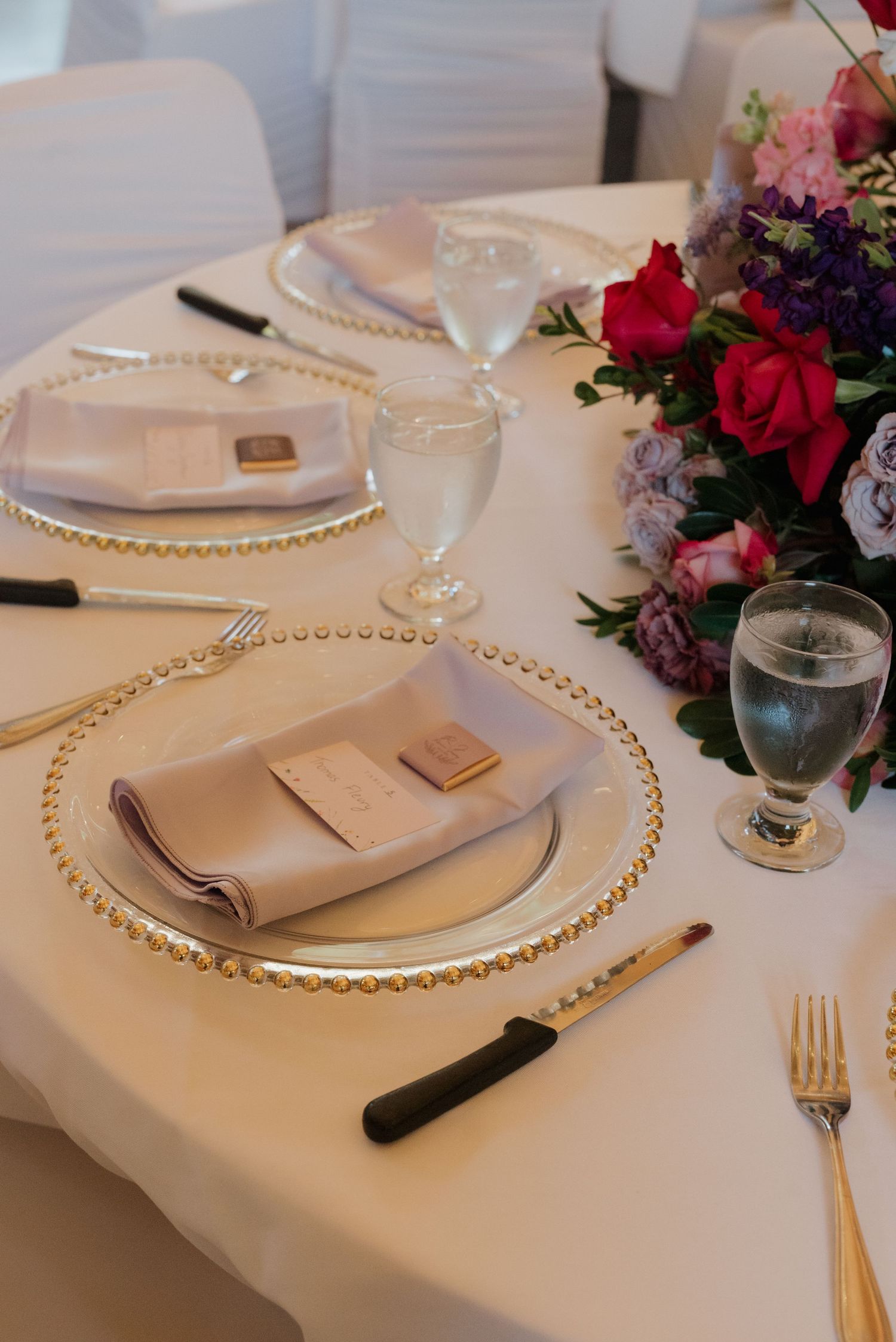Elegant wedding table settings with beaded charger plates, white linens, and colorful floral centerpieces.