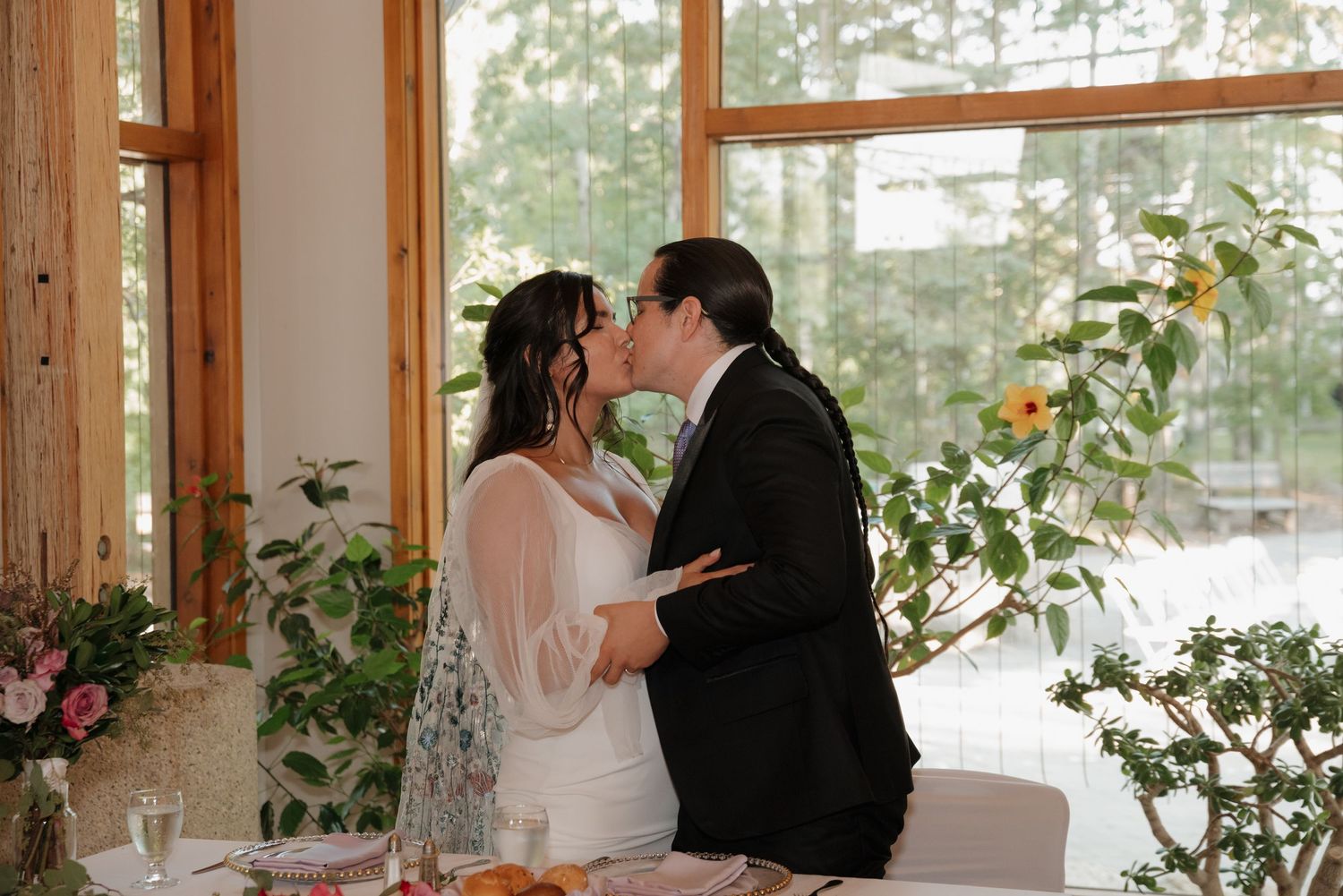 A romantic wedding scene in a bright sunlit venue with wooden beams and floral decorations.