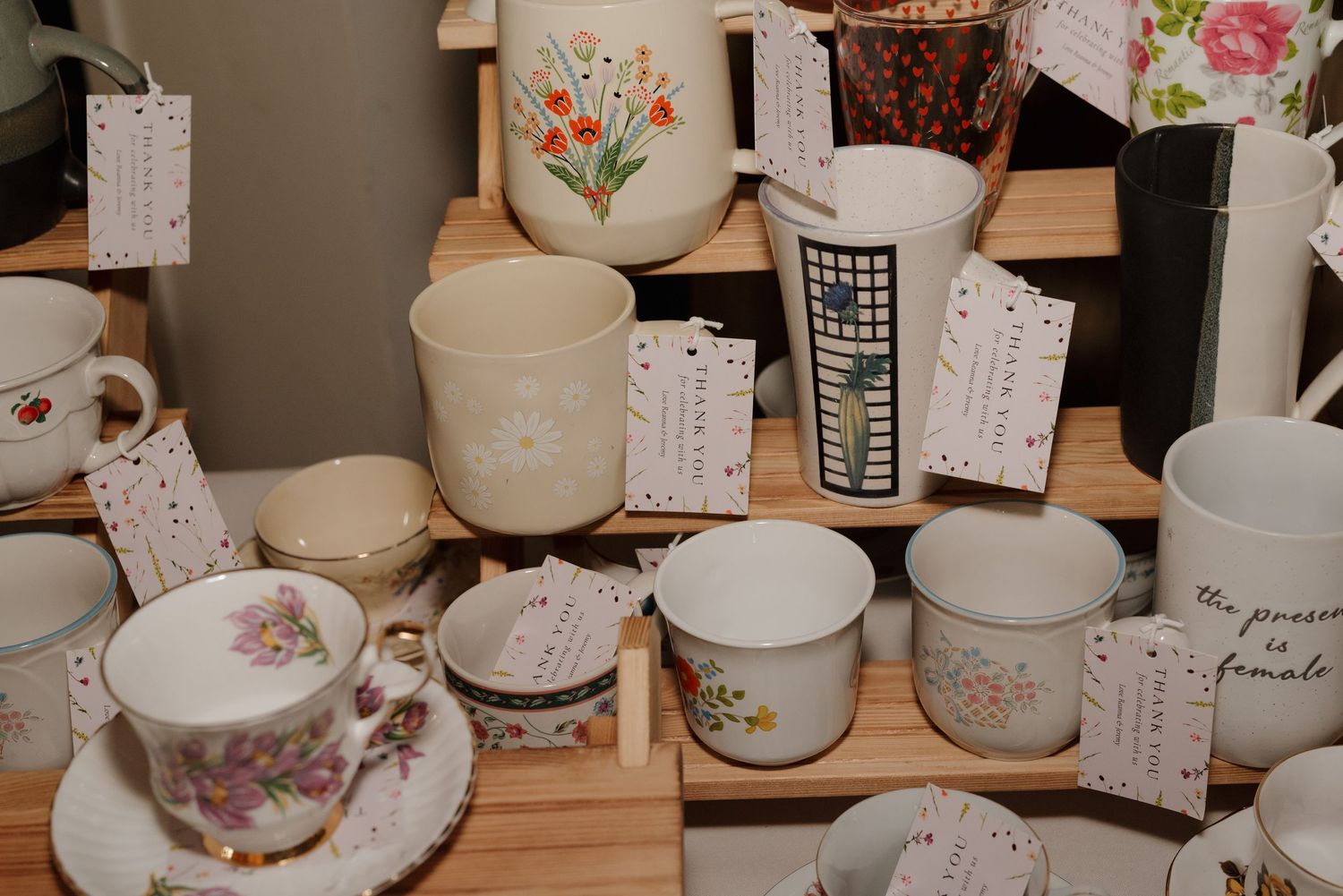Display of vintage teacups and mugs with floral designs and price tags on wooden shelf.