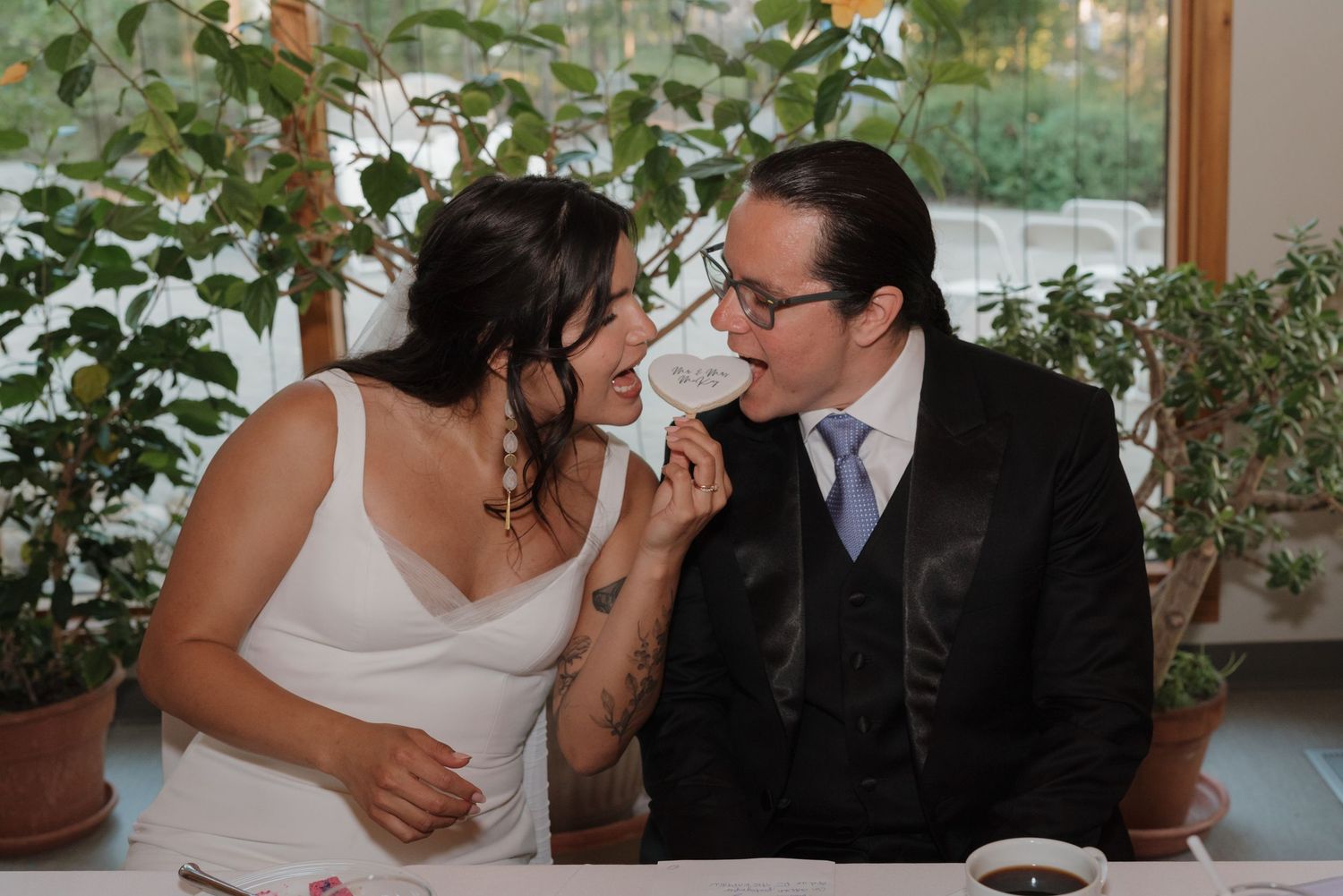 Wedding celebration scene with guests gathered in an indoor venue decorated with potted plants.