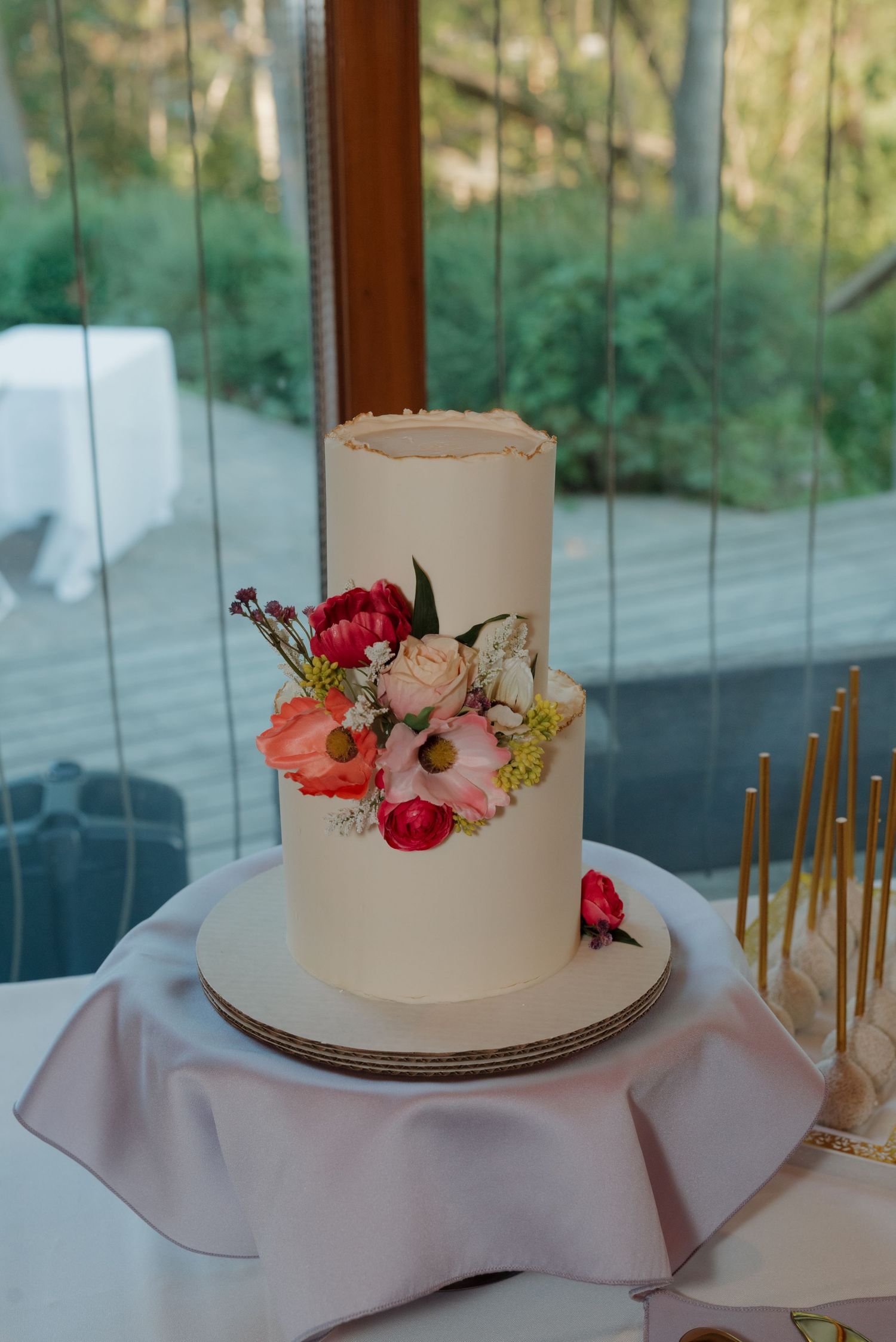 Simple white wedding cake decorated with fresh flowers in coral and pink tones on a light tablecloth.