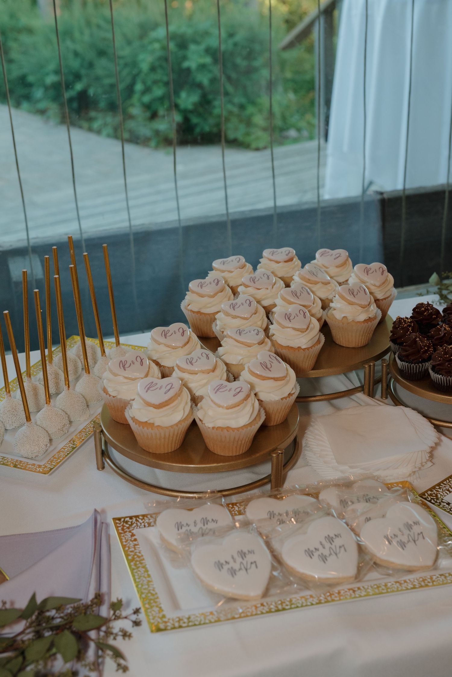 Elegant display of frosted cupcakes with gold candles on white serving plates at wedding dessert table.