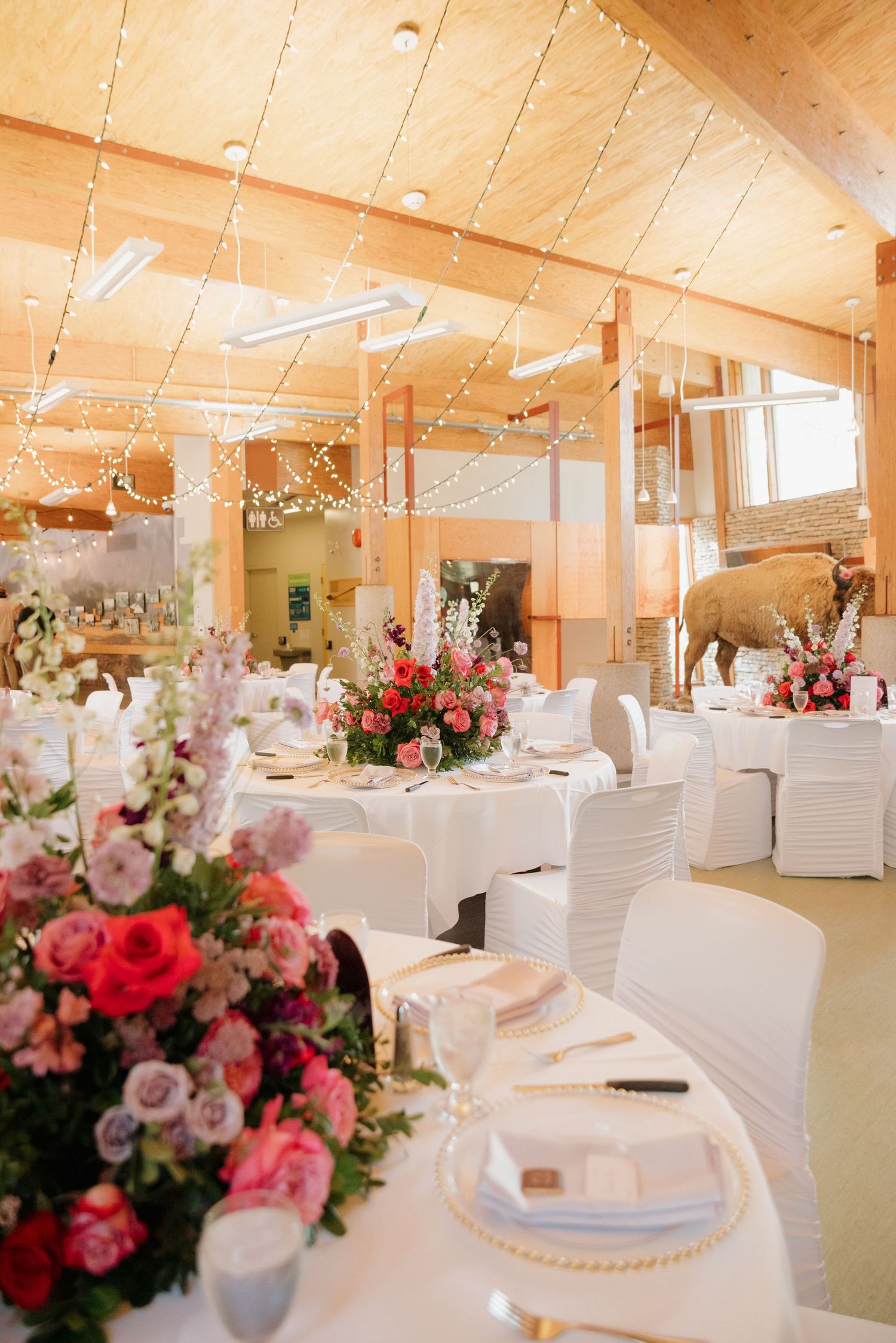 Elegant wedding reception venue with white chairs, floral centerpieces, and wooden beam ceiling in warm lighting.