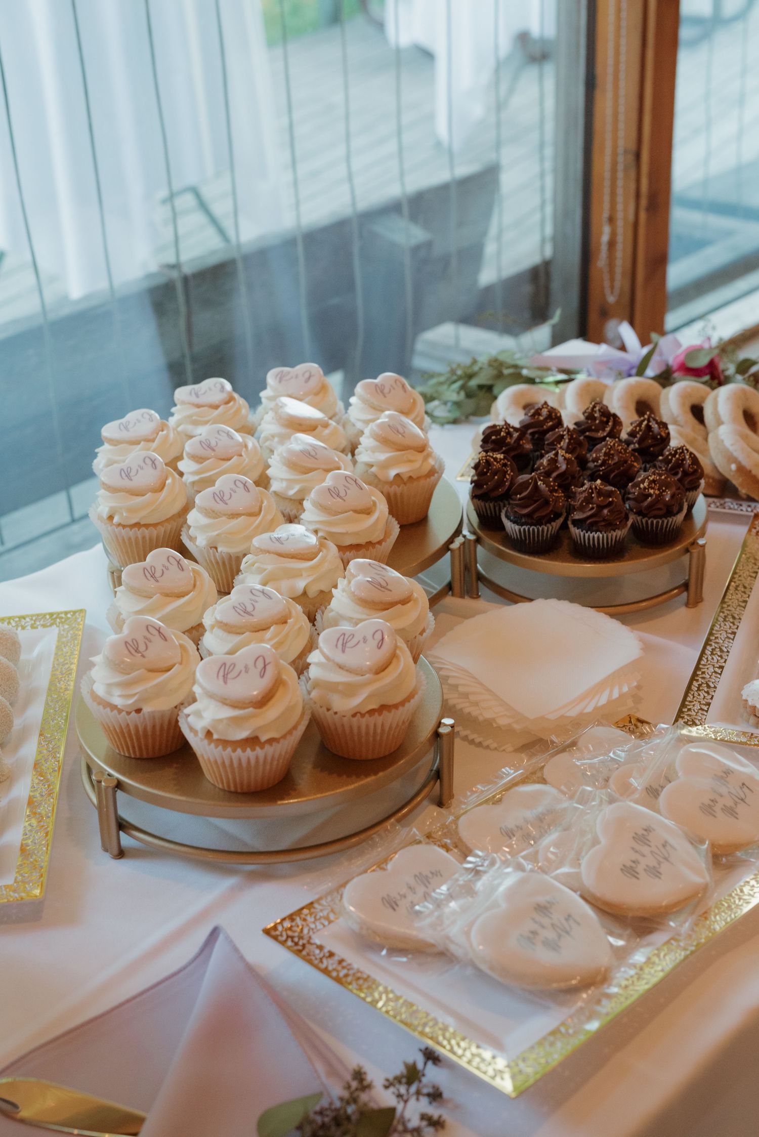 Wedding dessert table with pink frosted cupcakes and heart-shaped cookies on decorative stands.