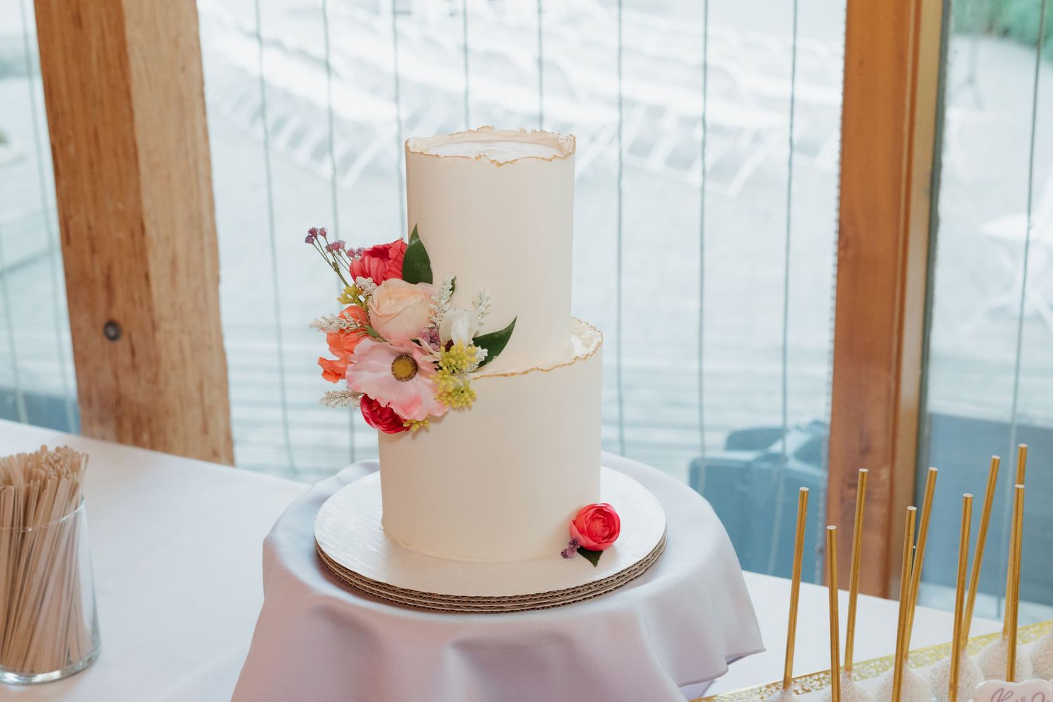 Elegant white wedding cake decorated with fresh pink and red roses on a white tablecloth.