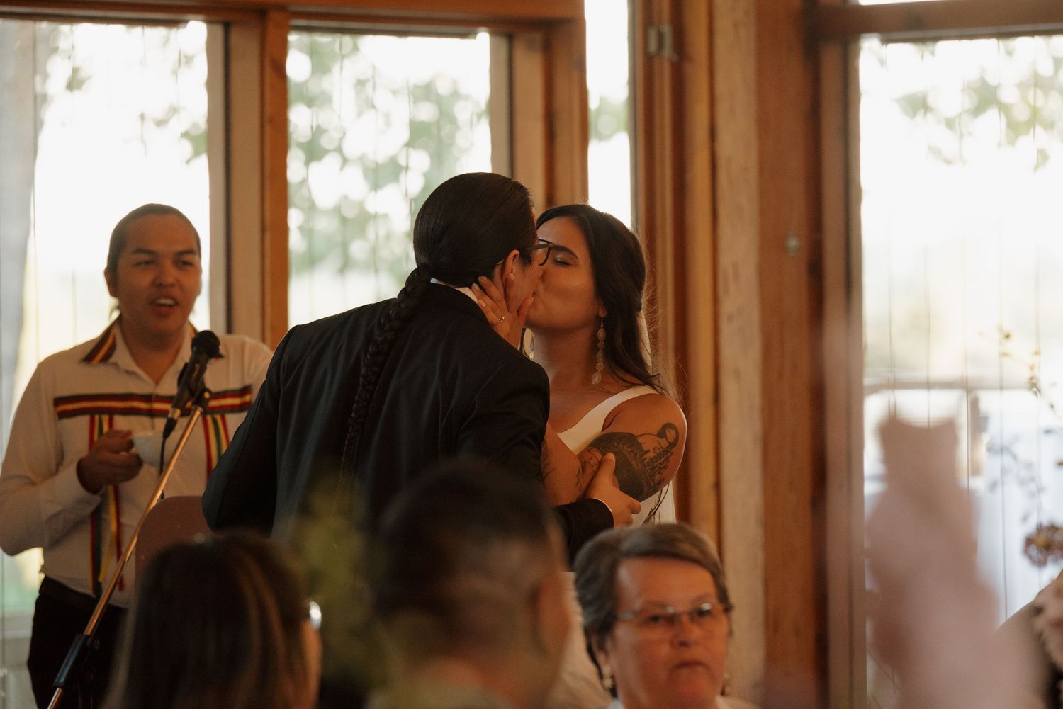 People gathered at a rustic indoor venue with wooden walls and windows, socializing and enjoying drinks together.