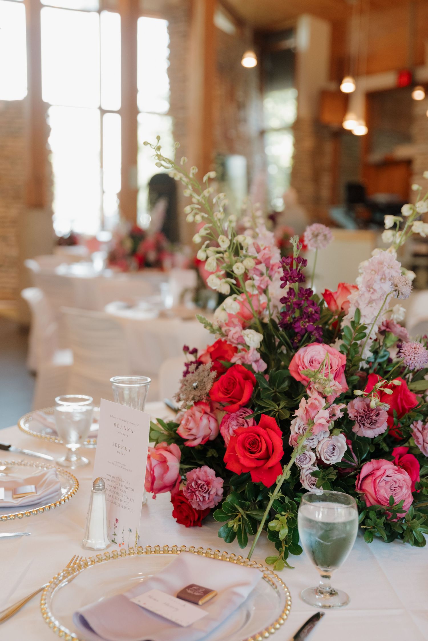 Elegant wedding table setting with pink and red floral centerpieces and gold-rimmed charger plates.