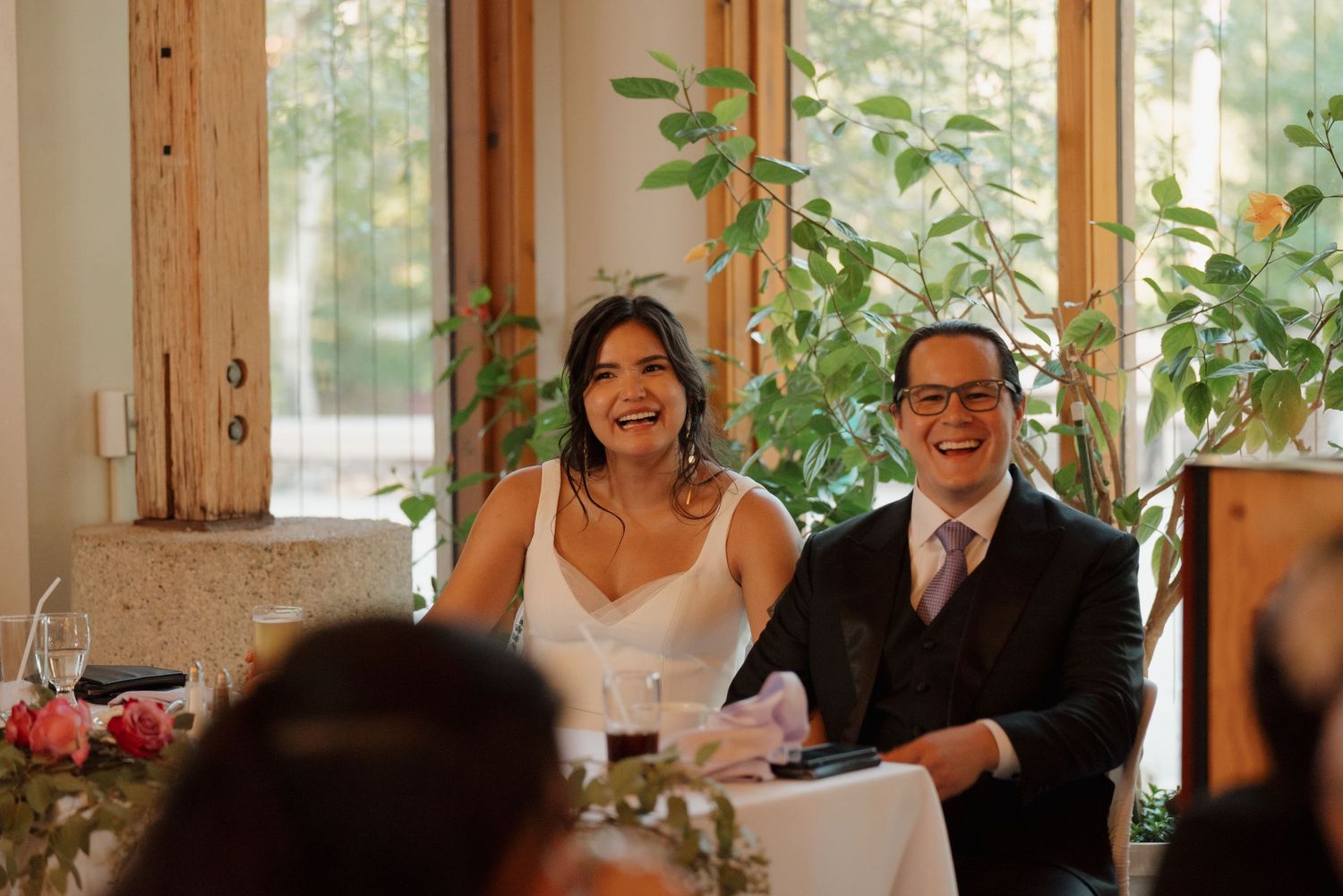 Wedding celebration in a rustic wooden venue with natural lighting and greenery decorations.