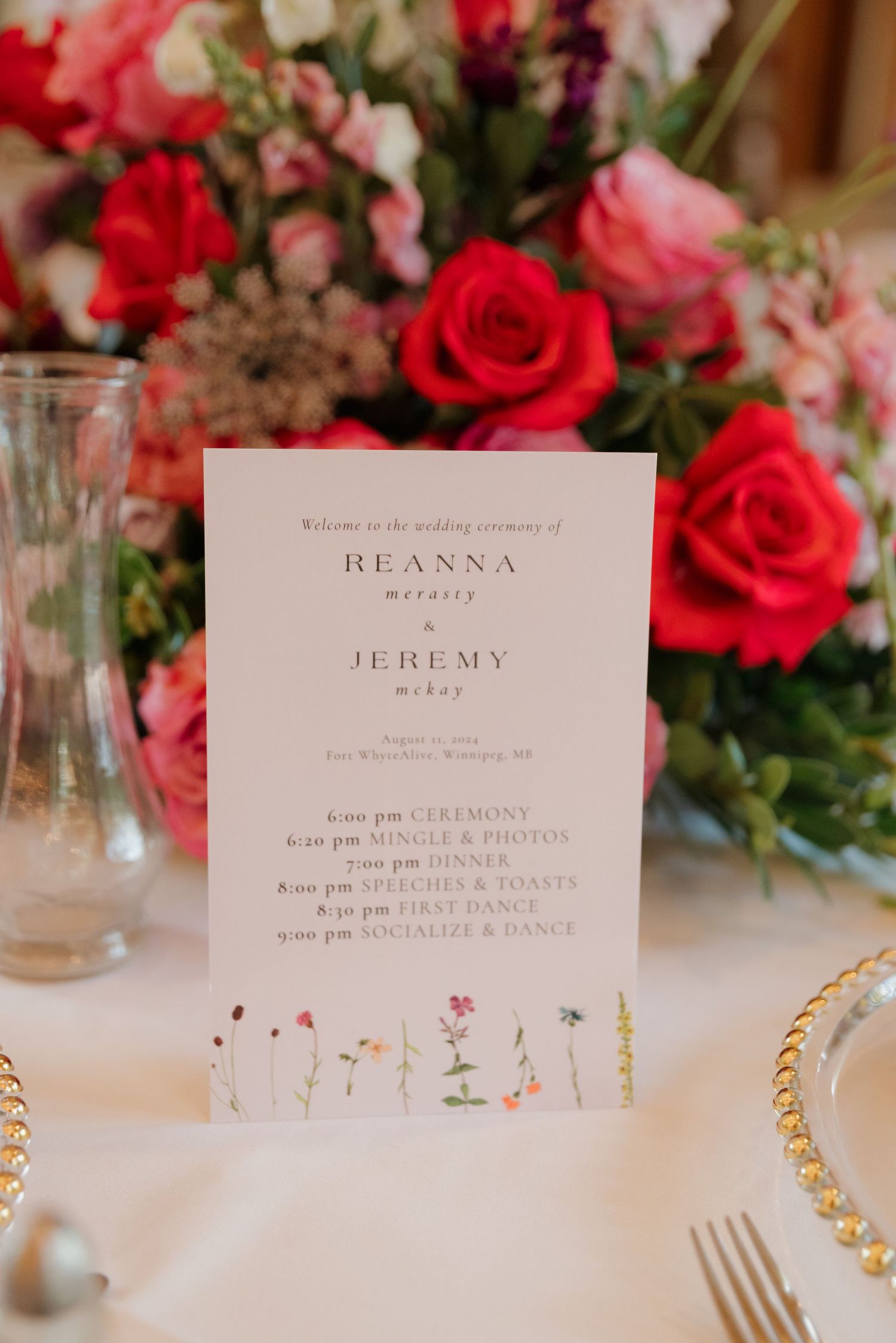 Wedding reception place cards and menu details displayed with vibrant red and pink floral arrangements.