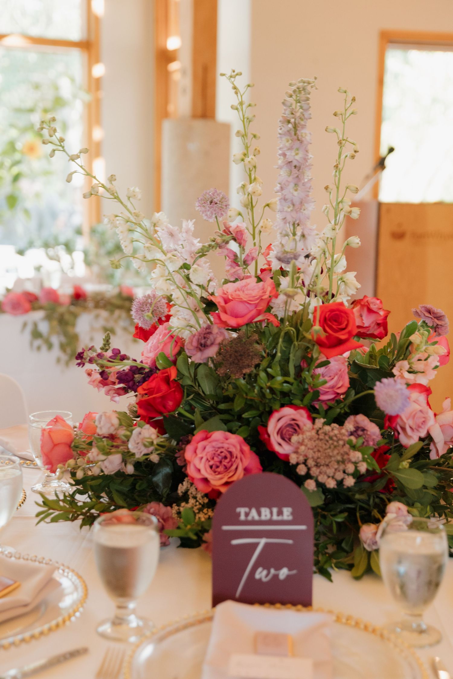 Elegant wedding table centerpieces featuring pink and red roses with delicate purple flowers in silver vases.