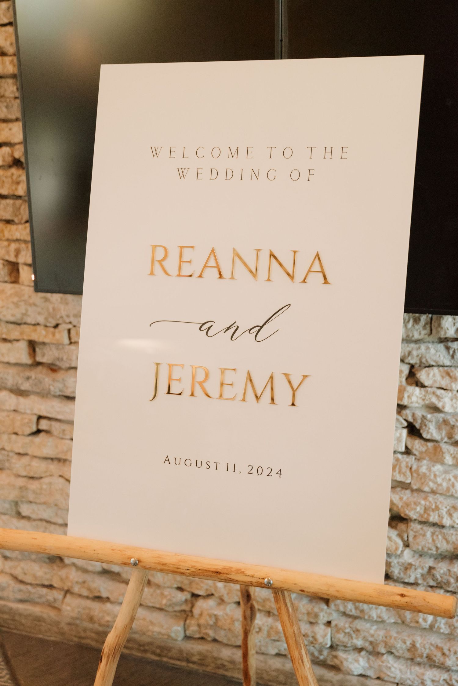 Elegant wedding welcome signs displayed on wooden easels with copper lettering against a rustic brick wall backdrop.