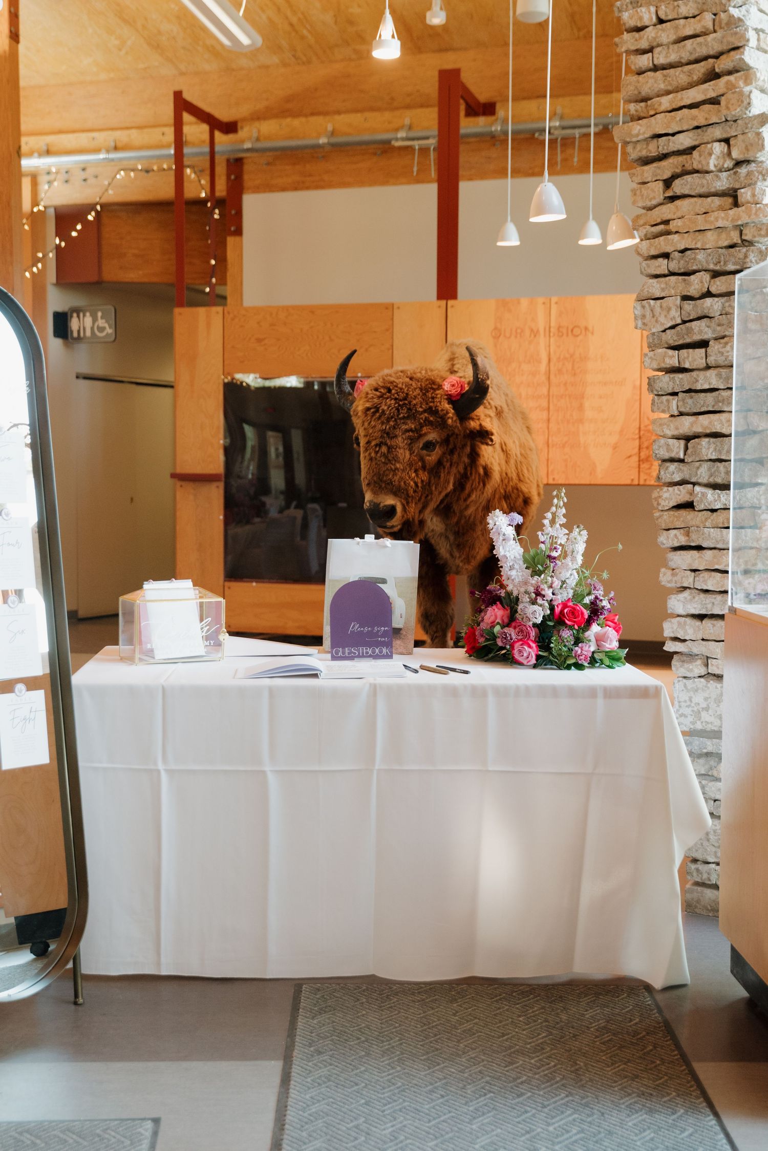 Reception venue with white-clothed tables and stone accent wall in rustic indoor setting.