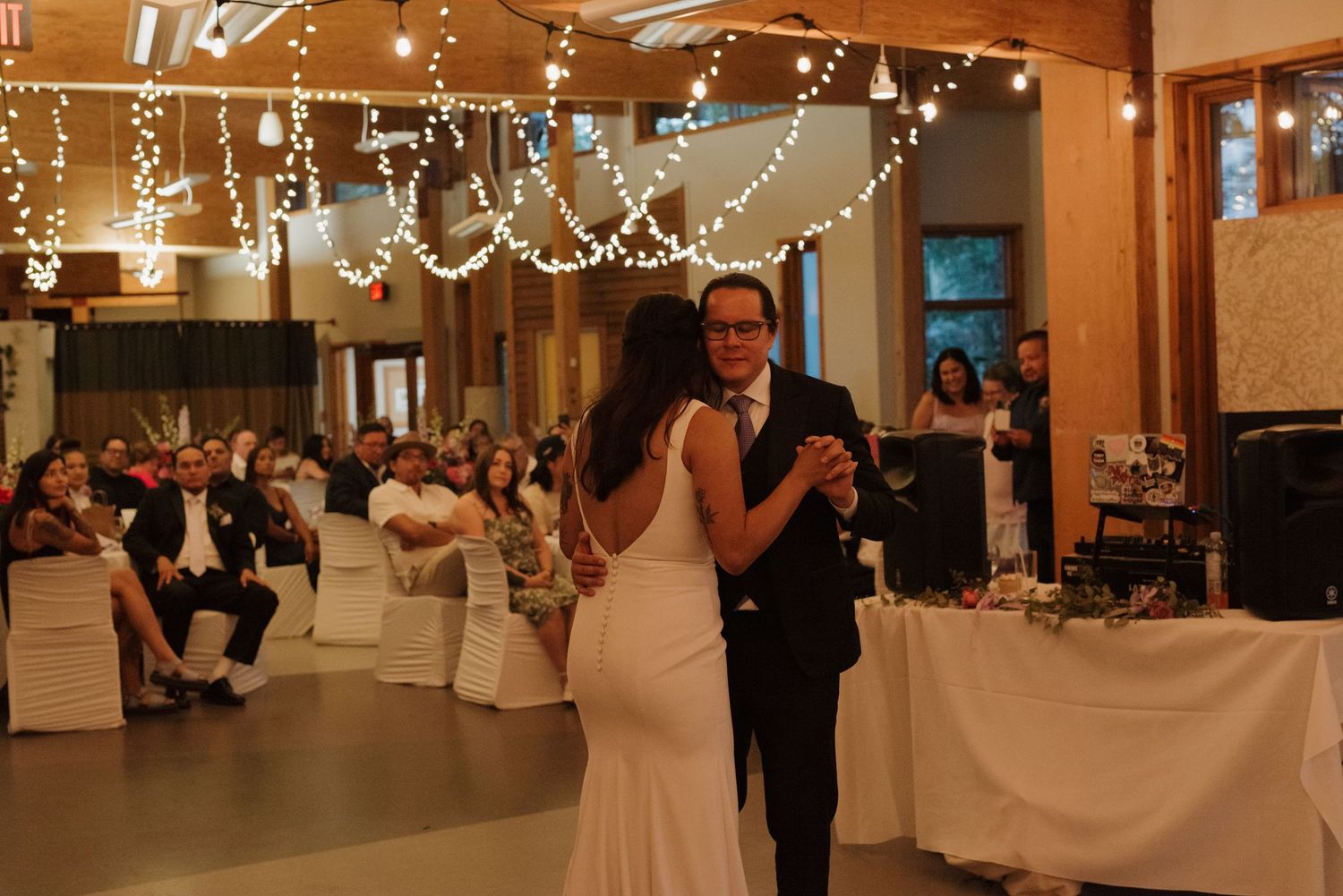 Indoor wedding reception venue decorated with hanging string lights and white tablecloths.