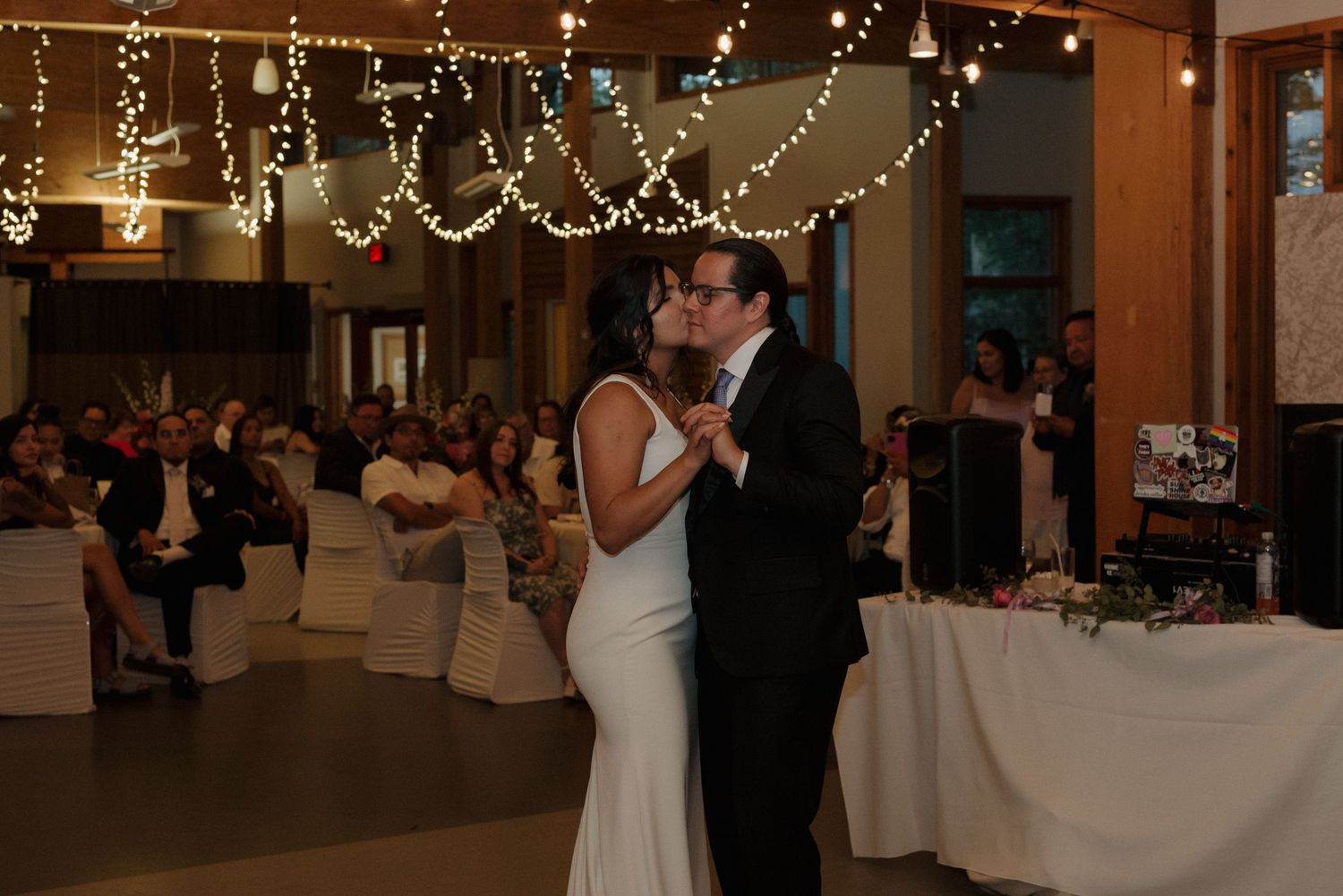 Wedding reception dance floor filled with guests dancing under string lights at an indoor venue.