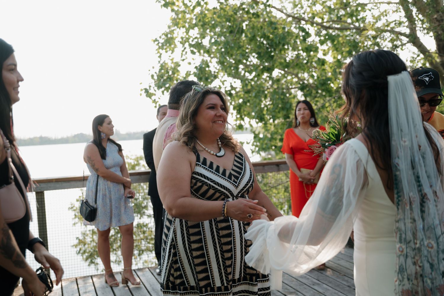 Outdoor gathering of wedding guests on a waterfront deck during celebration.