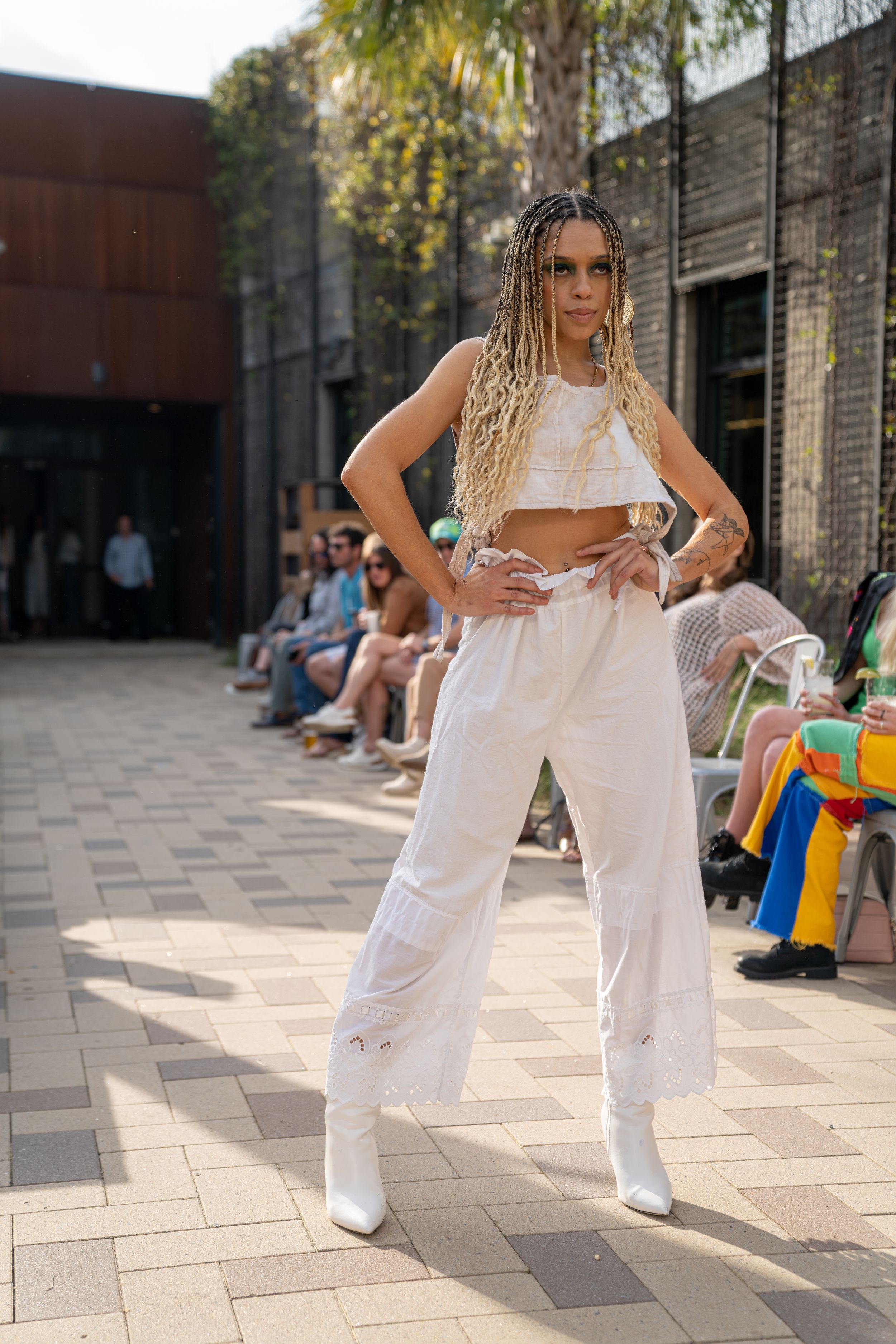 Person in white outfit performing dance moves on an outdoor patio with brick buildings in background.