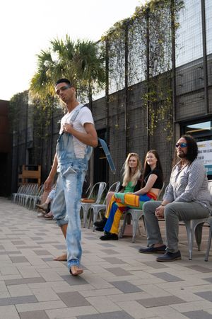 A group of people relaxing outdoors on chairs while someone performs a dance move on a tiled patio area.