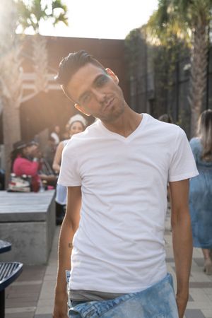 Person in white t-shirt and jeans poses casually against urban backdrop with palm trees.
