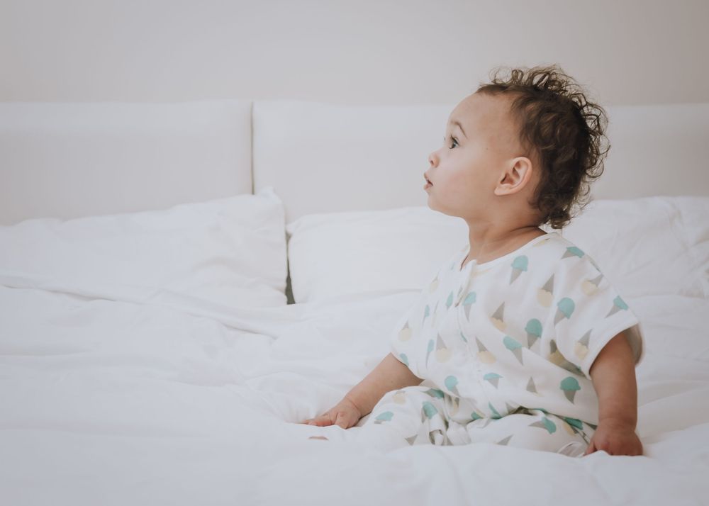 Baby sleeping peacefully on white bedding while wrapped in a floral swaddle blanket.