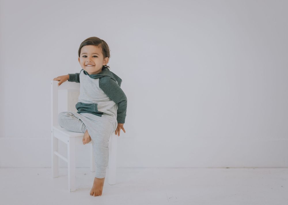 A child wearing a green and gray outfit plays and moves dynamically against a white background.