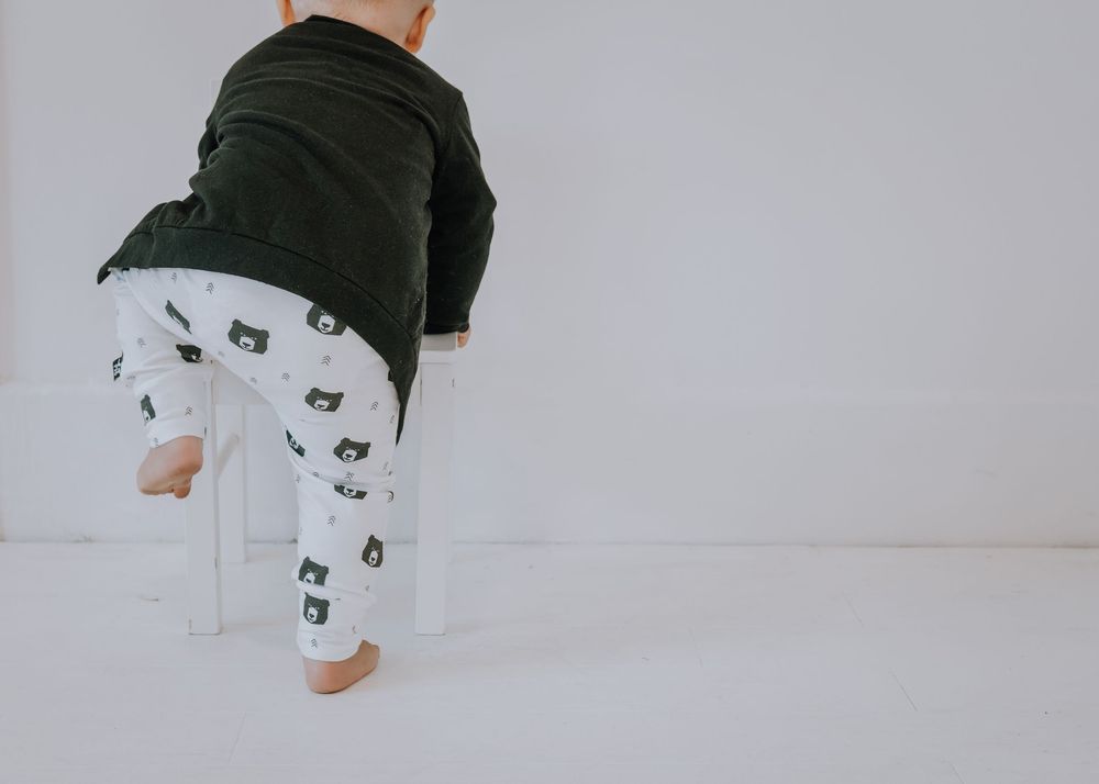 Minimalist white and green baby clothing items laid out in a row against a light background.