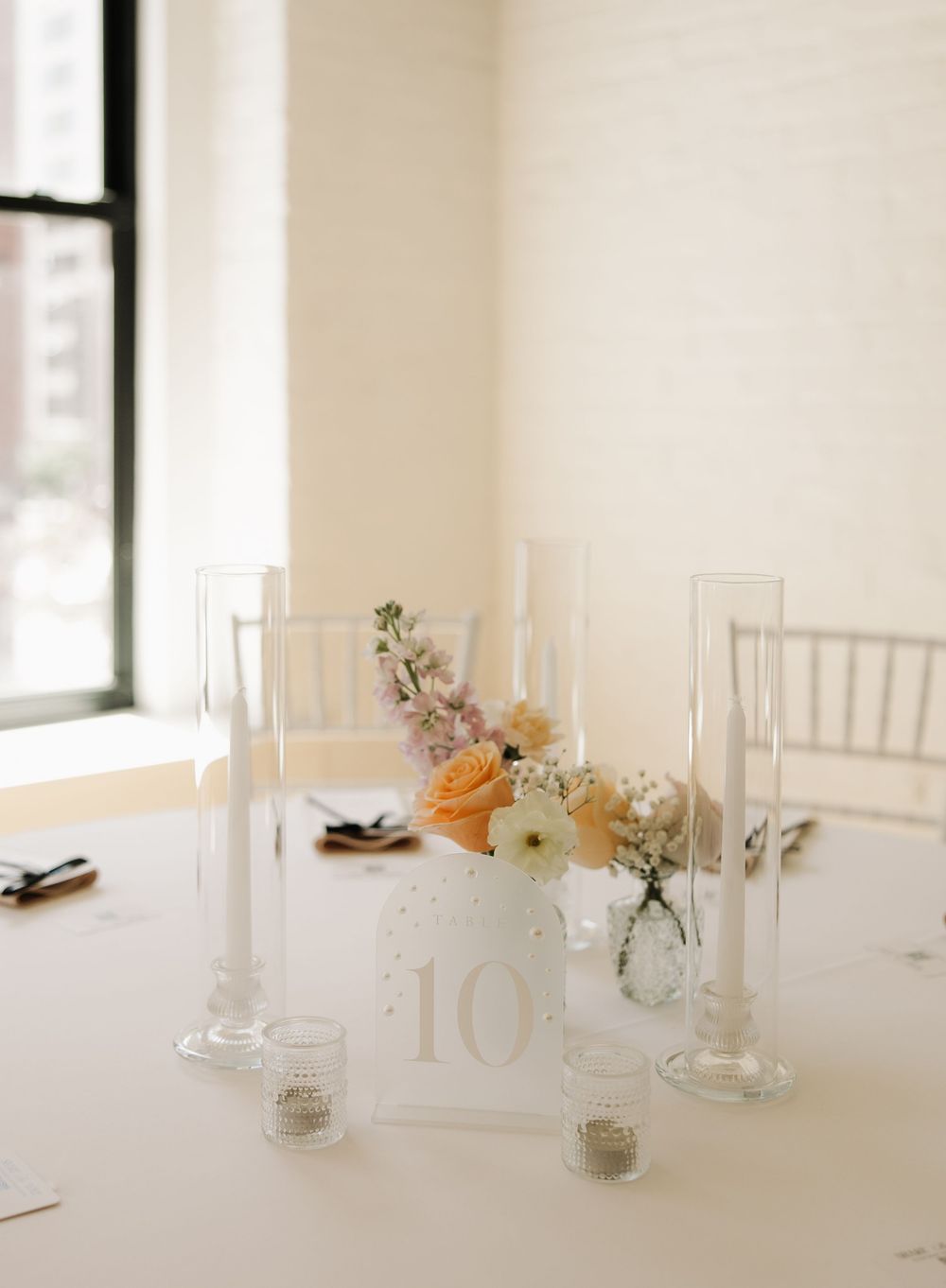 An elegant white wedding table setting with floral centerpieces and tall glass candleholders.
