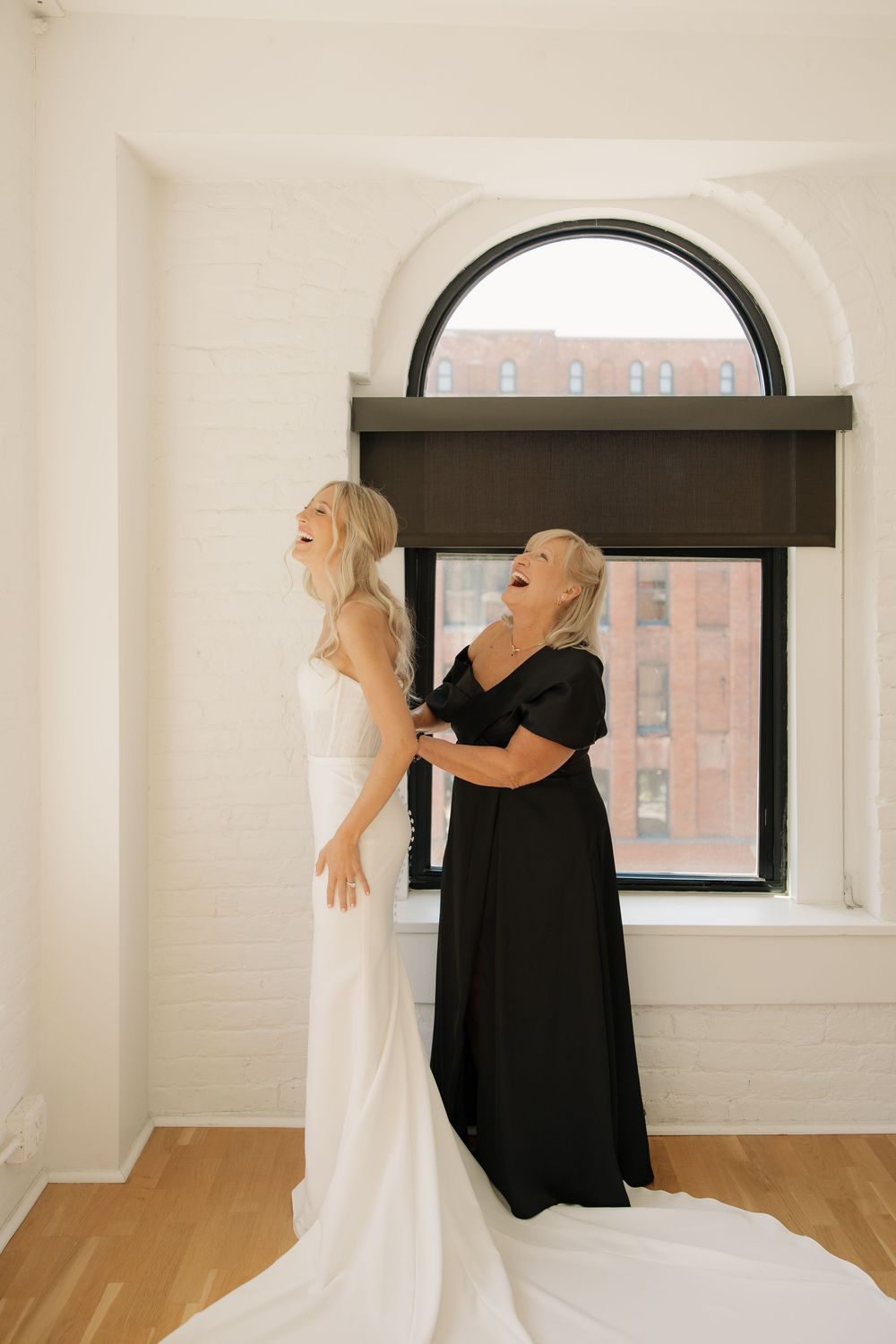 Two people in contrasting white and black outfits dance gracefully in a bright minimalist studio with arched windows.
