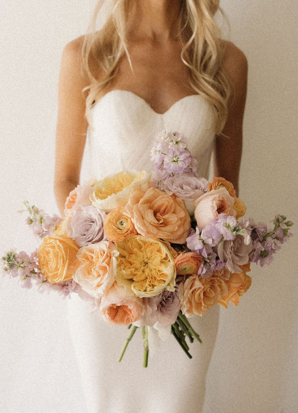 A white wedding dress adorned with a delicate floral arrangement of peach and lavender blooms along the neckline.
