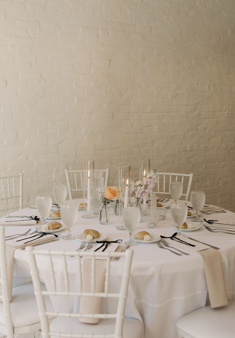 Elegant wedding reception tables set with white linens, chiavari chairs, and minimal place settings in a bright venue.