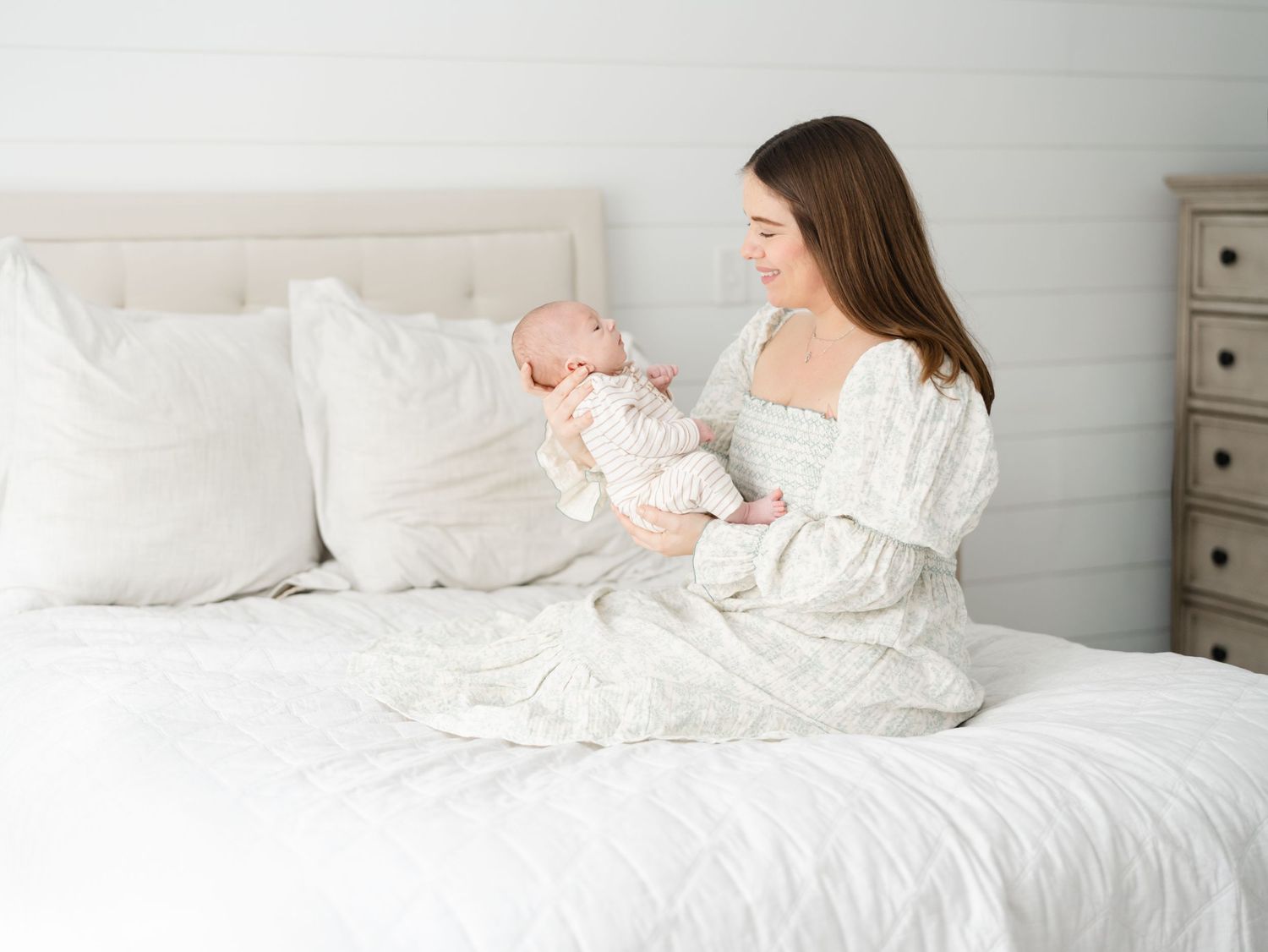 Mother holding newborn sitting on master bed in-home newborn session in NJ.