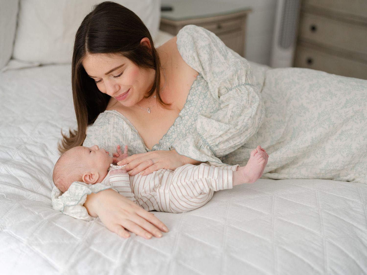 Mother laying on bed with newborn smiling down at him during a lifestyle in home newborn photo session in Monmouth County.