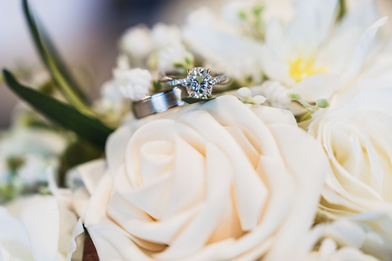 A sparkling engagement ring with blue stones sits atop delicate white roses in a wedding bouquet.