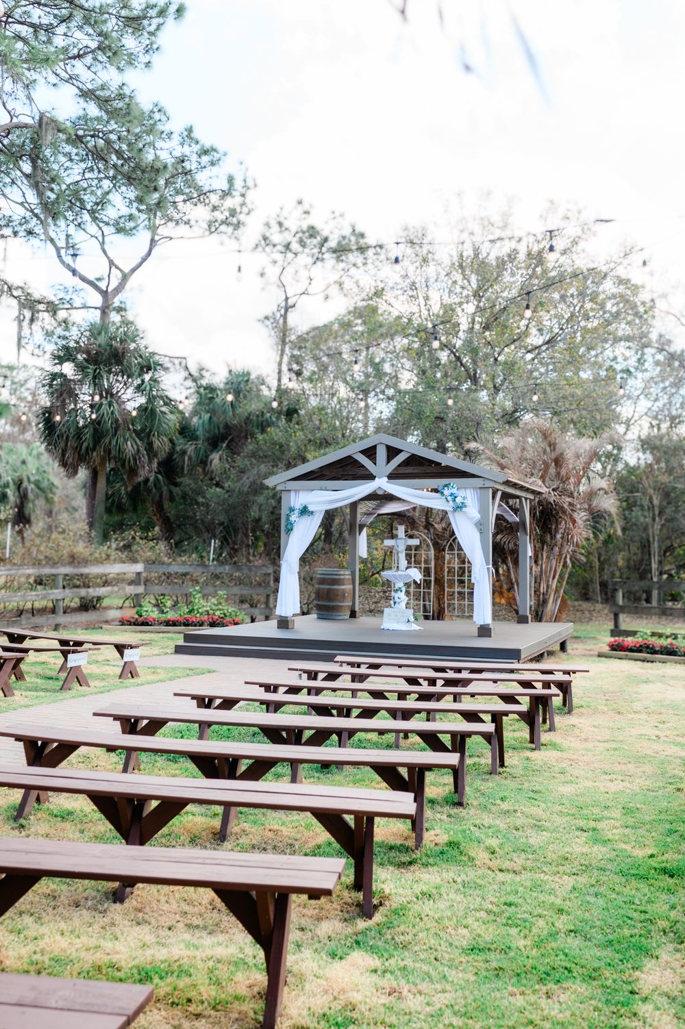 Rows of wooden picnic tables arranged on grass leading to a white pavilion decorated with fabric draping for an outdoor event.