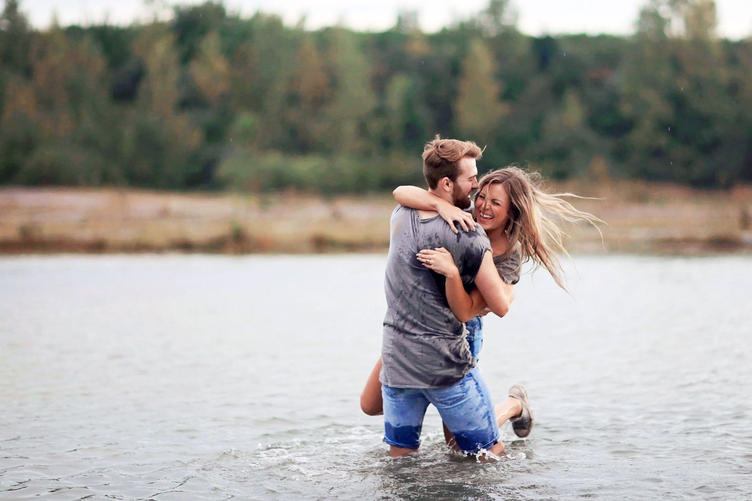 A couple embraces while playing in shallow water at sunset, creating romantic silhouettes against the lake.