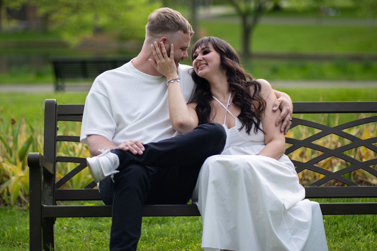 A romantic couple shares a tender moment on a park bench surrounded by lush greenery and natural scenery.